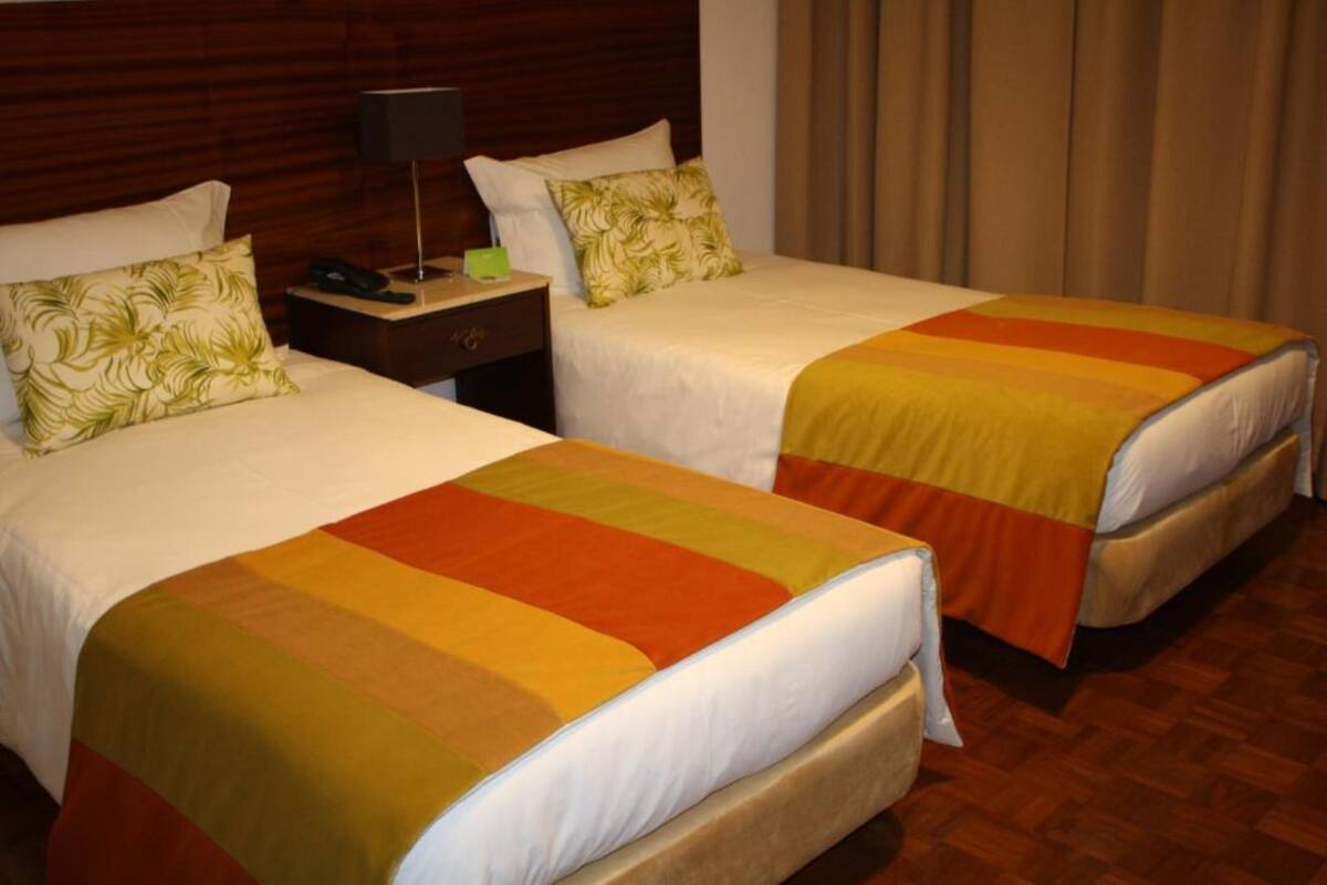 Two beds with matching headboards, a bedside table with a lamp, and a telephone.