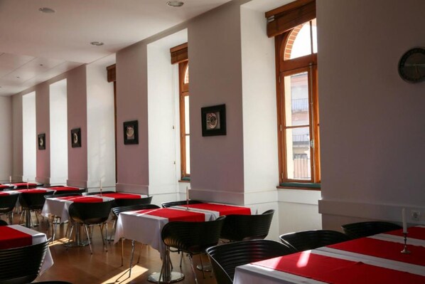 Un comedor con mesas y sillas, ventanas amplias y cuadros en las paredes.