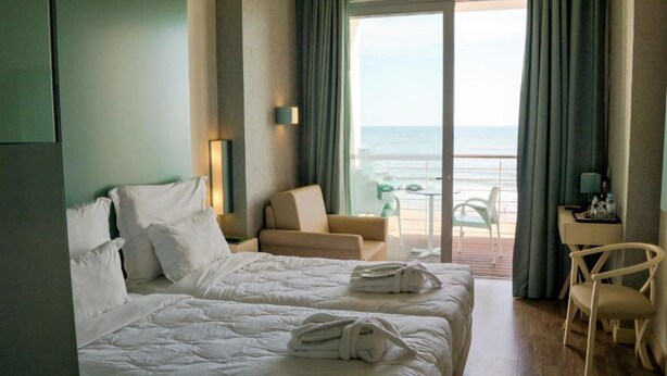Habitación de hotel con dos camas, un sofá, una silla y un balcón con vista al mar.