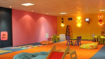 Une salle de jeux avec des meubles aux couleurs vives, un tapis de jeu et un téléviseur fixé au mur.