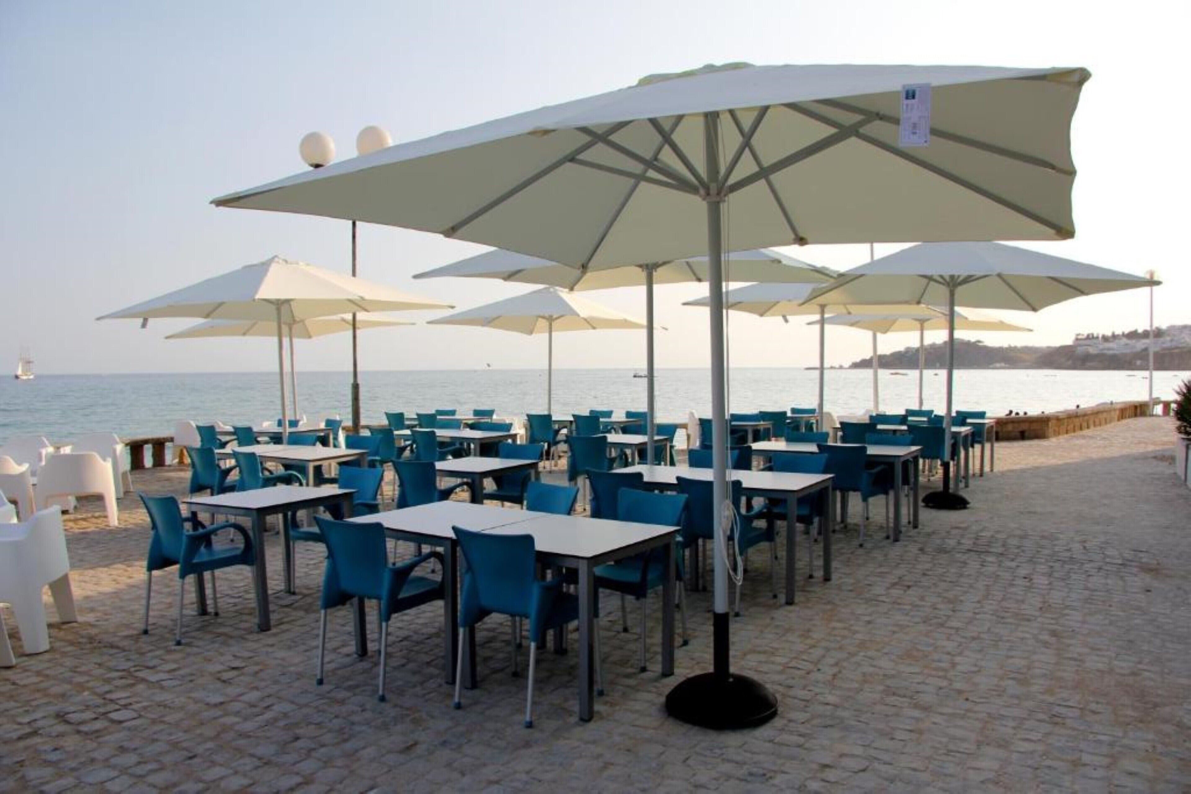 Terraza al aire libre con mesas, sillas, sombrillas y vista al mar.