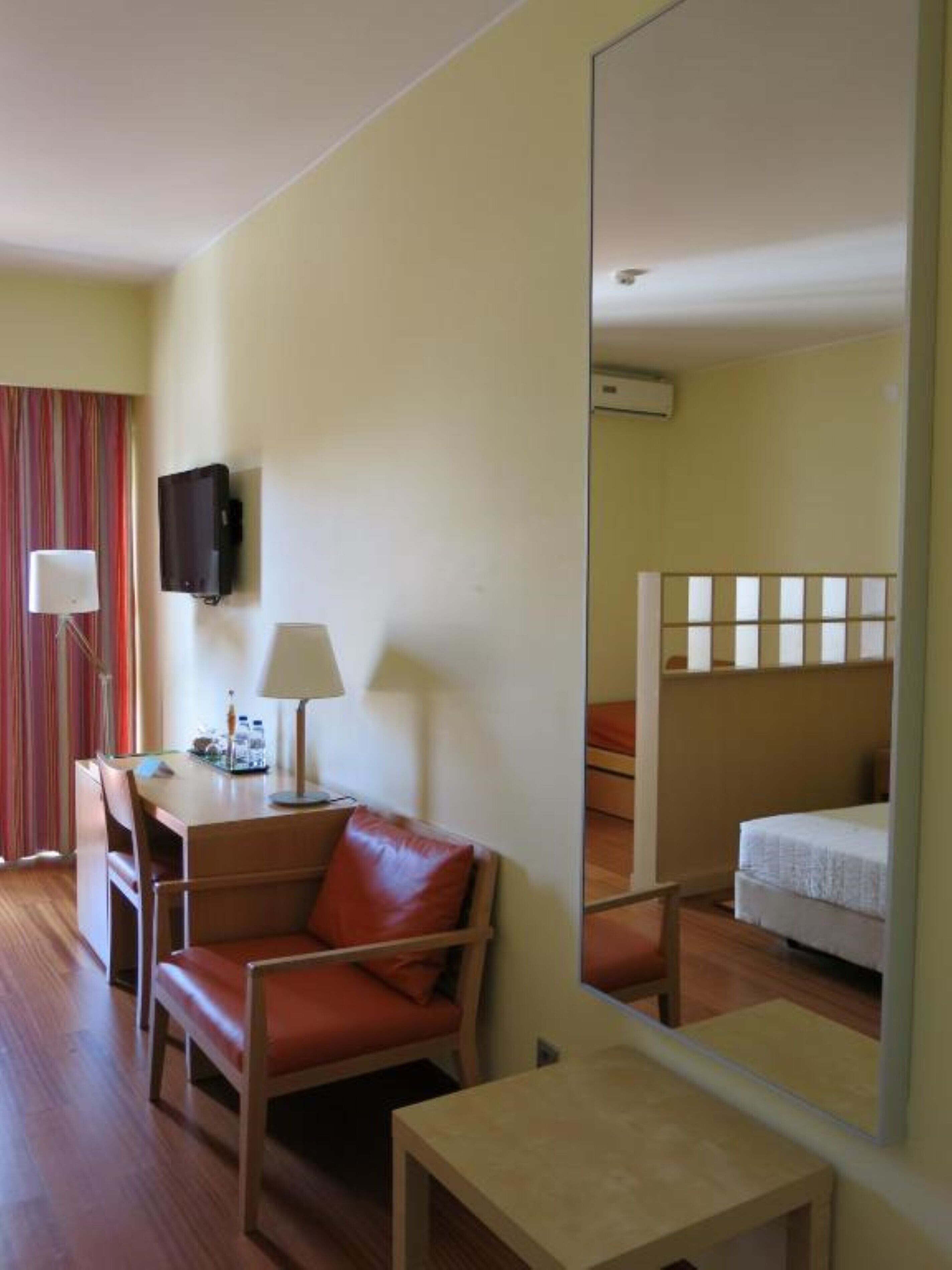 Une chambre d’hôtel avec un lit, un bureau, une chaise, une télévision et un miroir.
