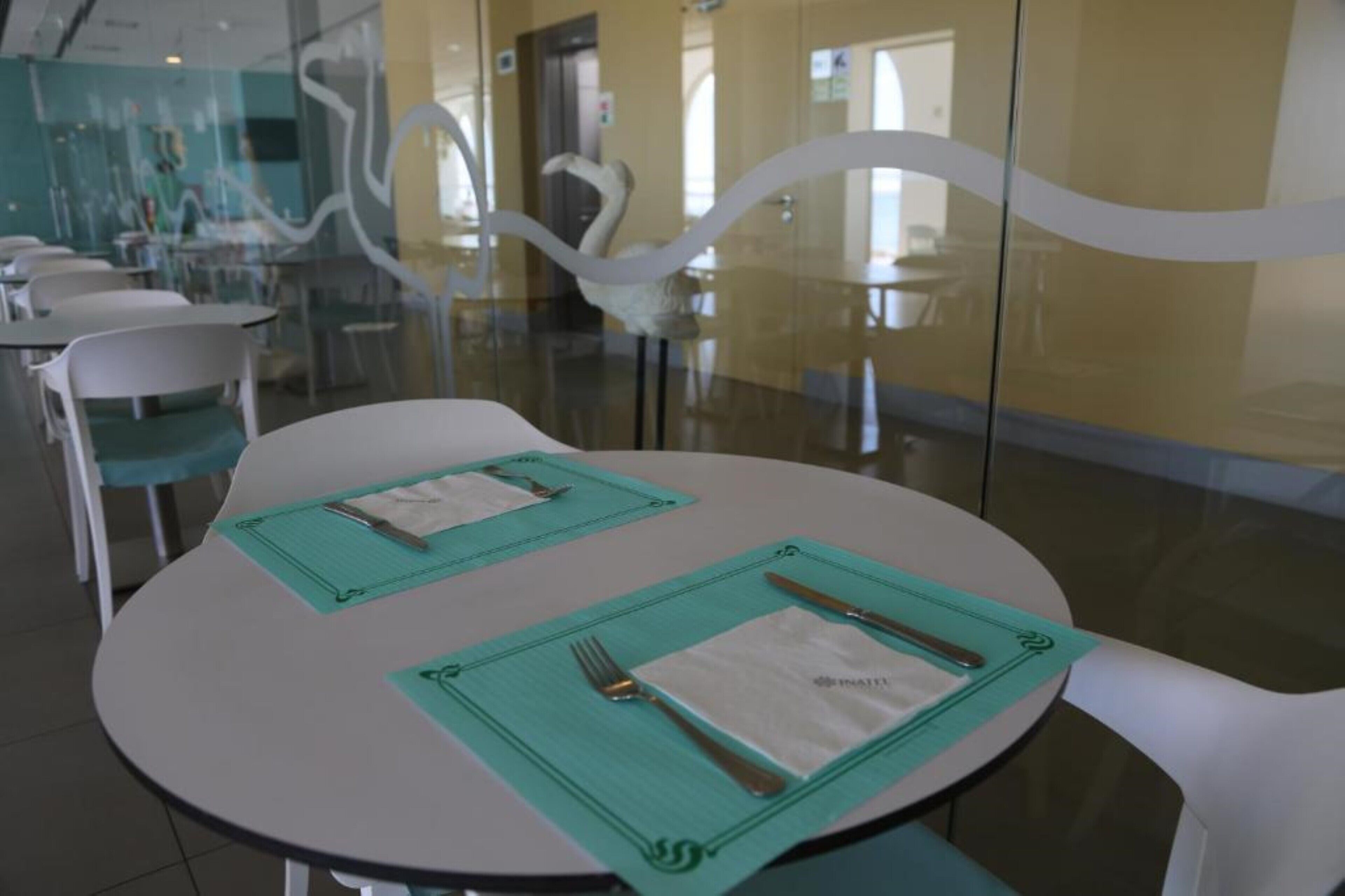 Un espace repas avec des tables rondes, chacune agrémentée d’un set de table vert, d’une serviette blanche et de couverts.