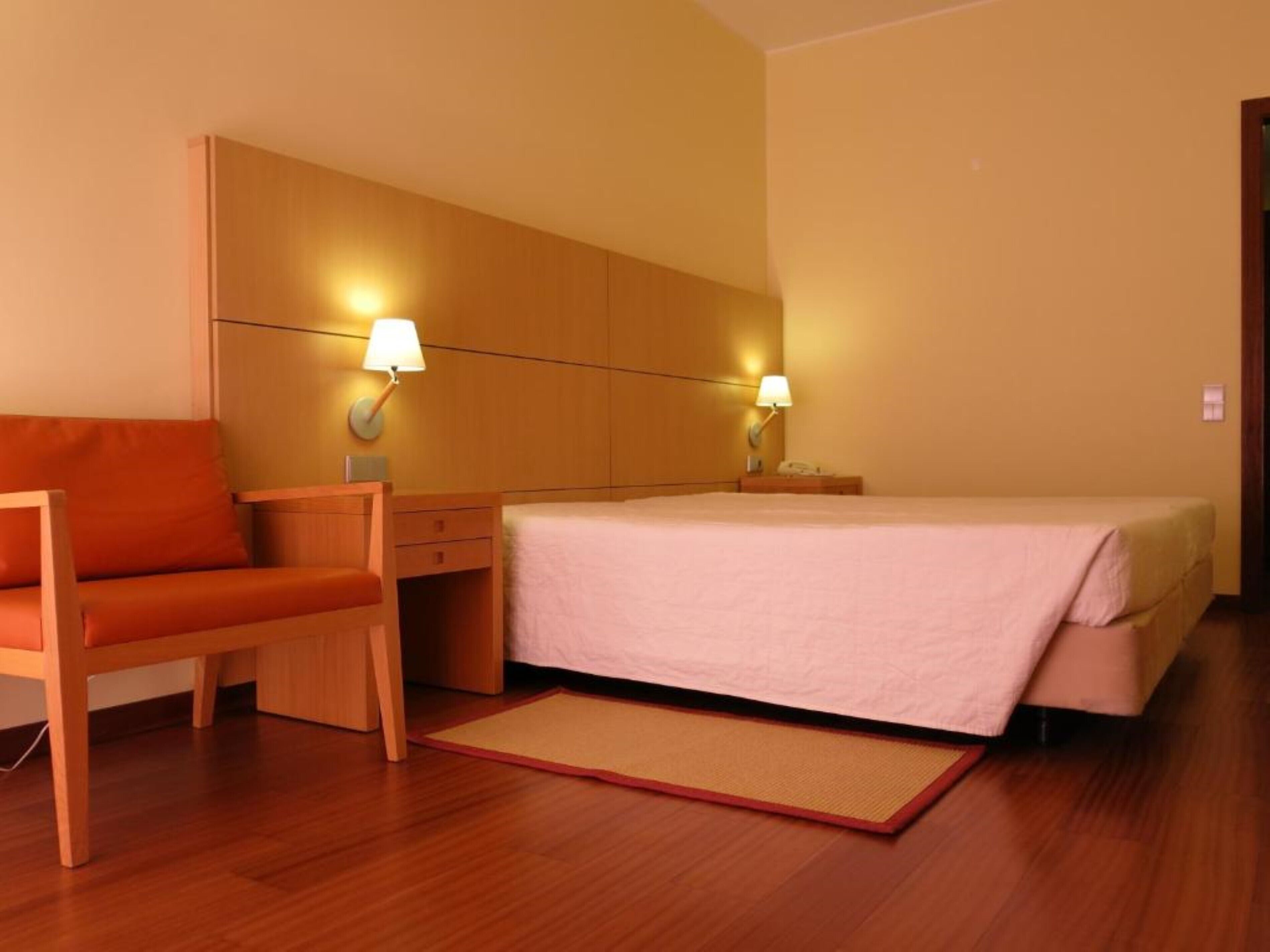 Una habitación de hotel con cama, escritorio, silla y dos lámparas de noche.