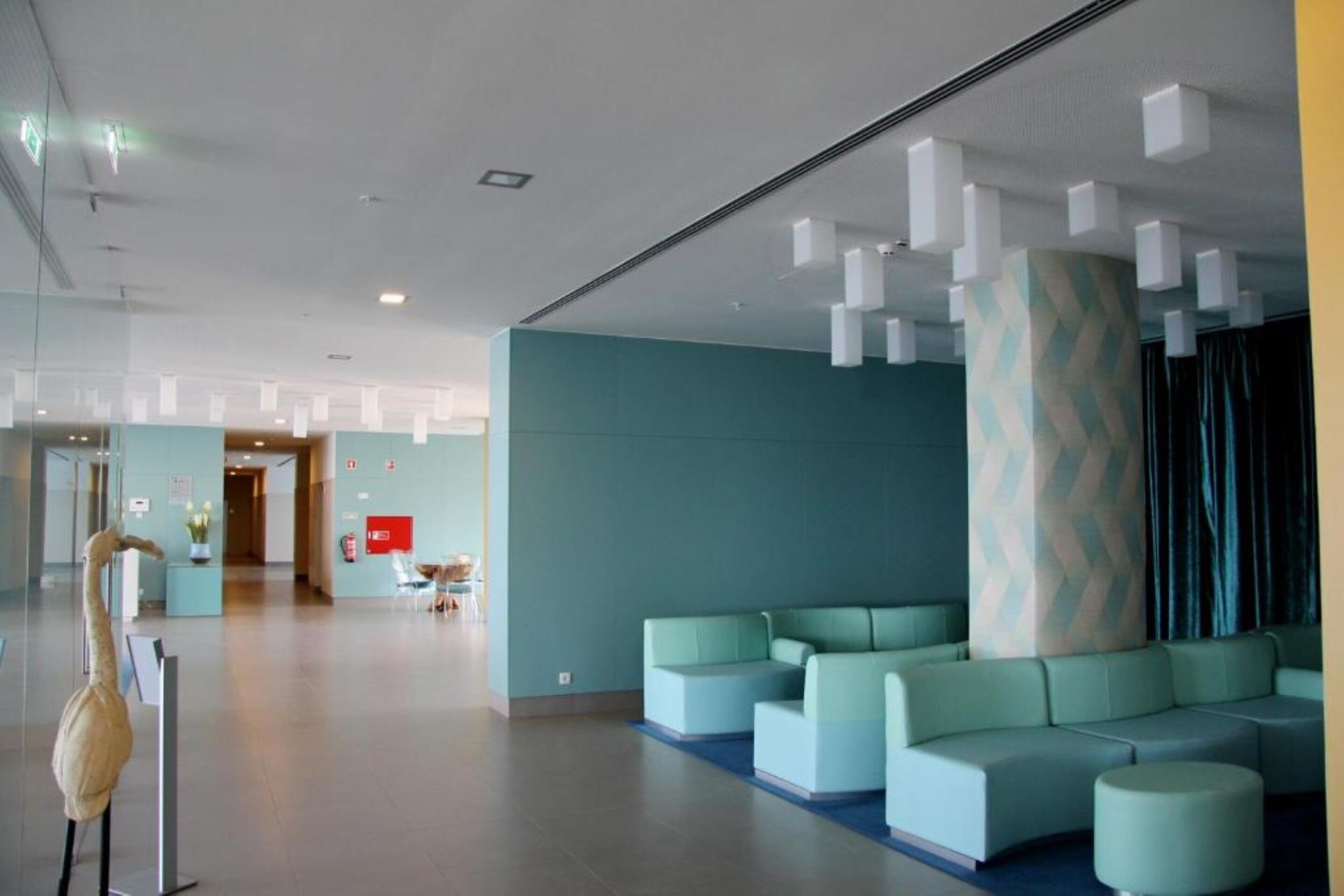 Un hall d’entrée moderne aux murs de couleur turquoise, agrémenté d’une grande colonne et de plusieurs espaces aménagés pour s’asseoir.