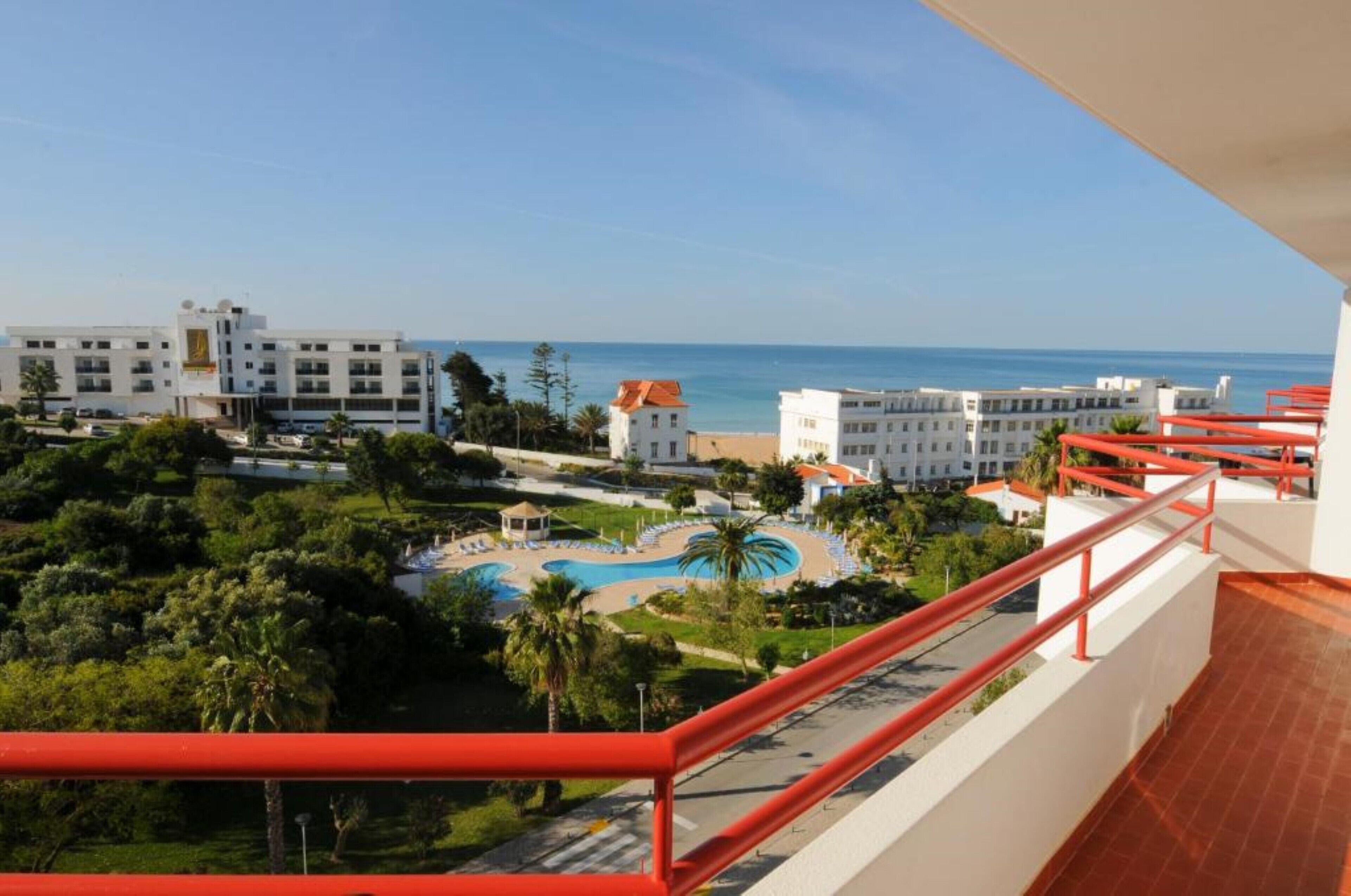 Un hotel con piscina, vista al mar y barandilla roja.