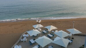 Un restaurante frente a la playa con terraza, sombrillas blancas y mesas.