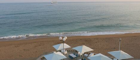 A beachside restaurant with outdoor seating, white umbrellas, and tables.