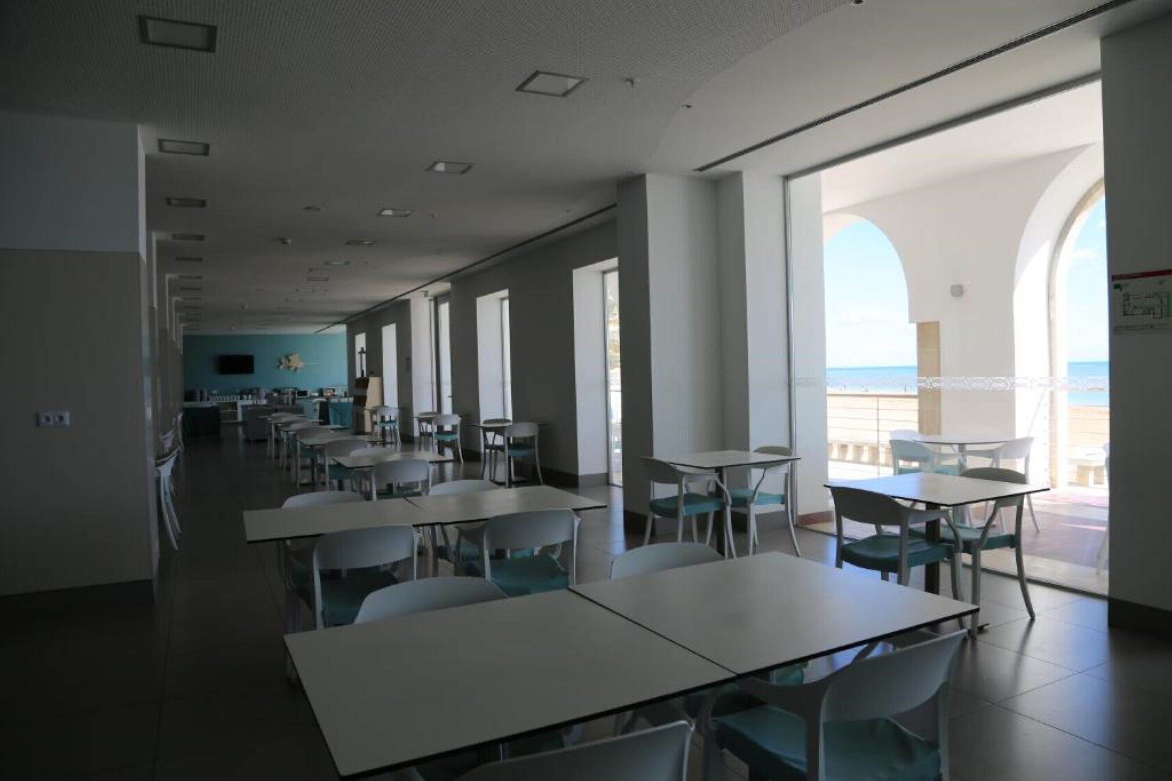 A spacious dining area with tables and chairs, large windows offering views of the sea, and a bright interior.
