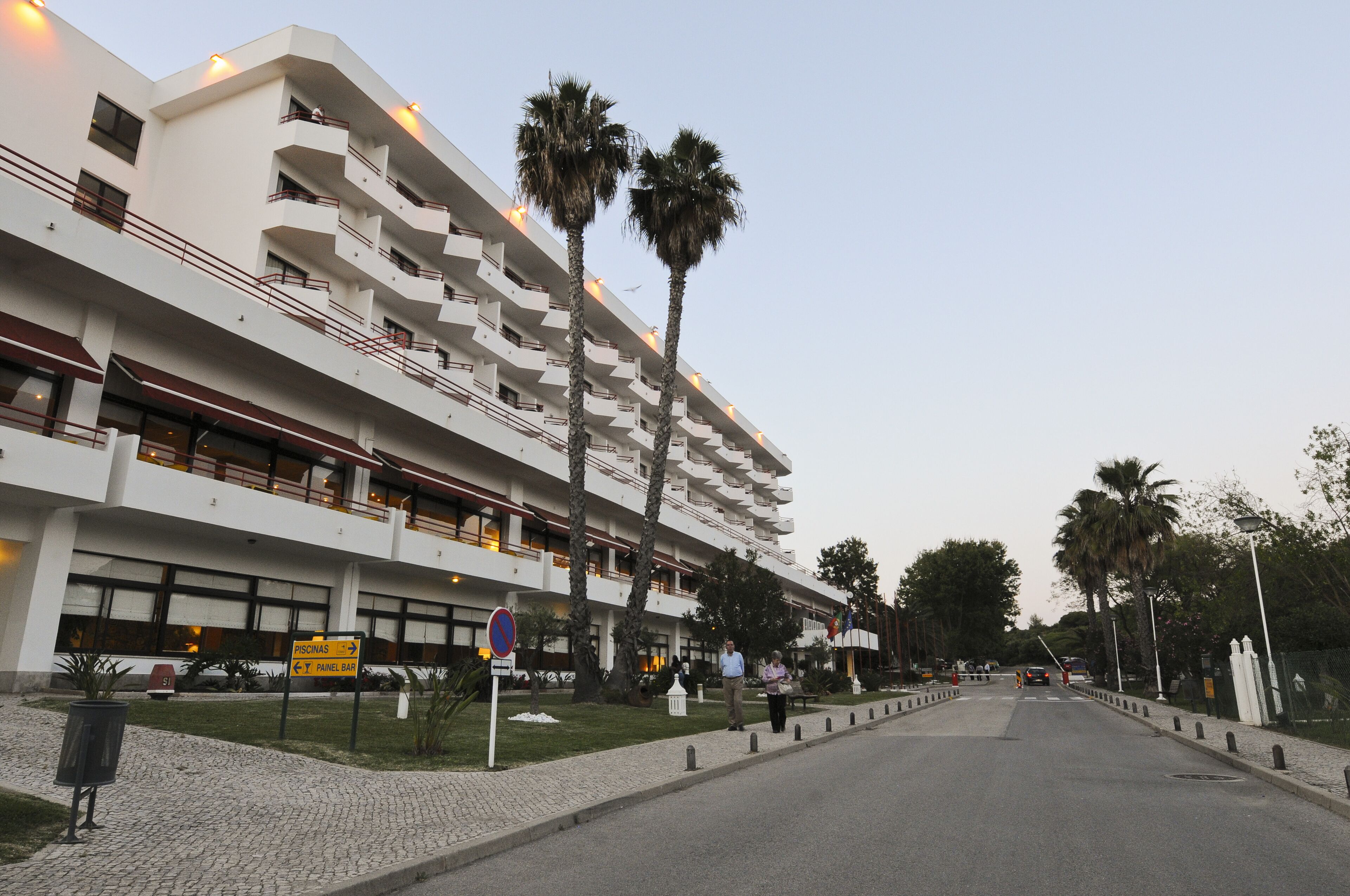 Un hotel de varios pisos con balcones, palmeras y un camino pavimentado.