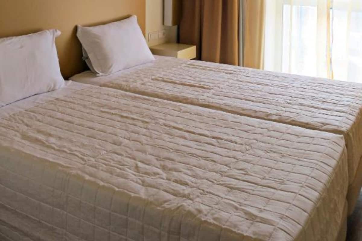 A hotel room with a large bed, two pillows, a nightstand, and a window with curtains.