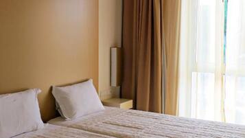 A hotel room with a large bed, two pillows, a nightstand, and a window with curtains.