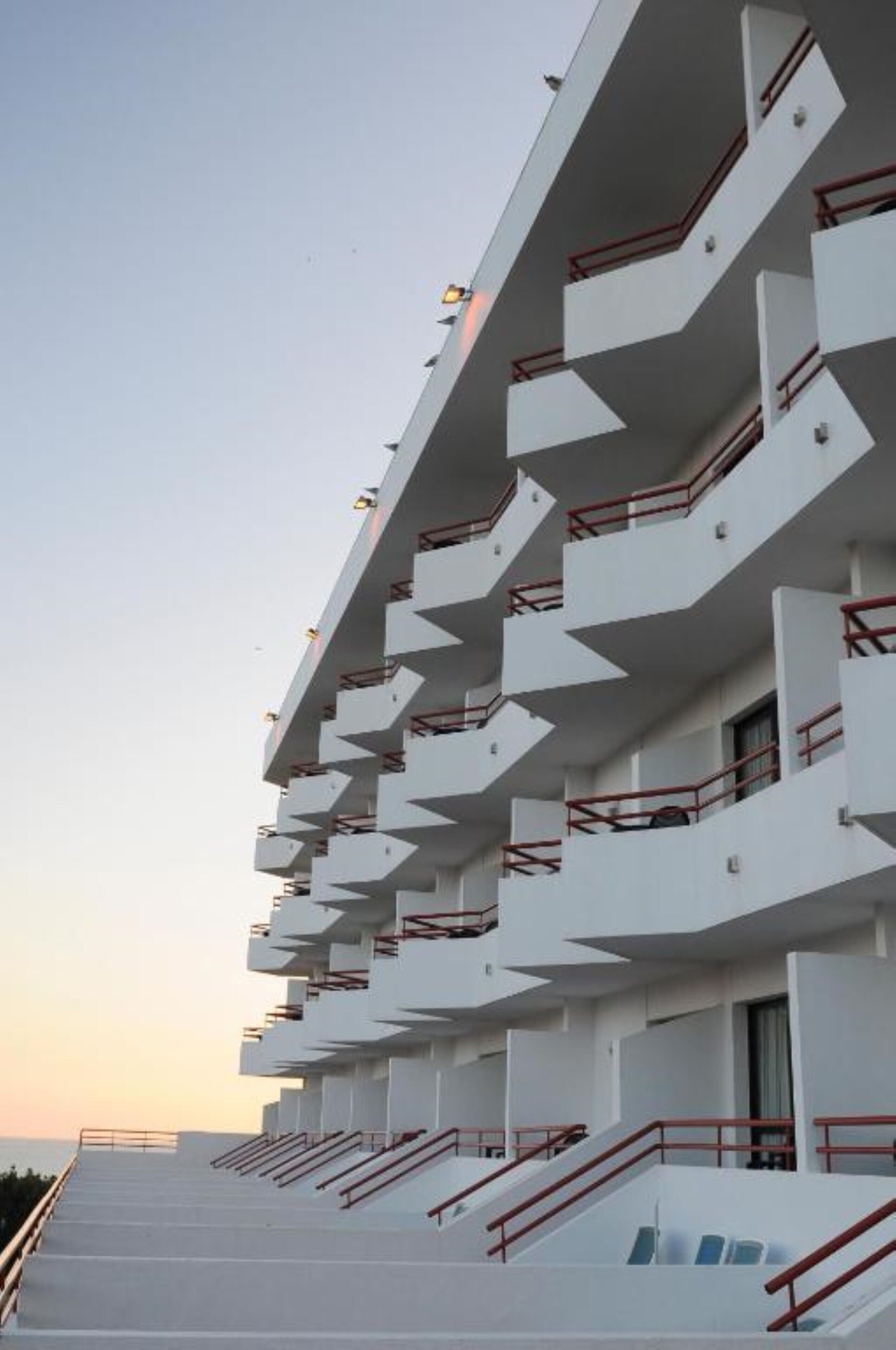 A multi-story hotel with a modern architectural design, featuring balconies and a staircase leading to the upper levels.