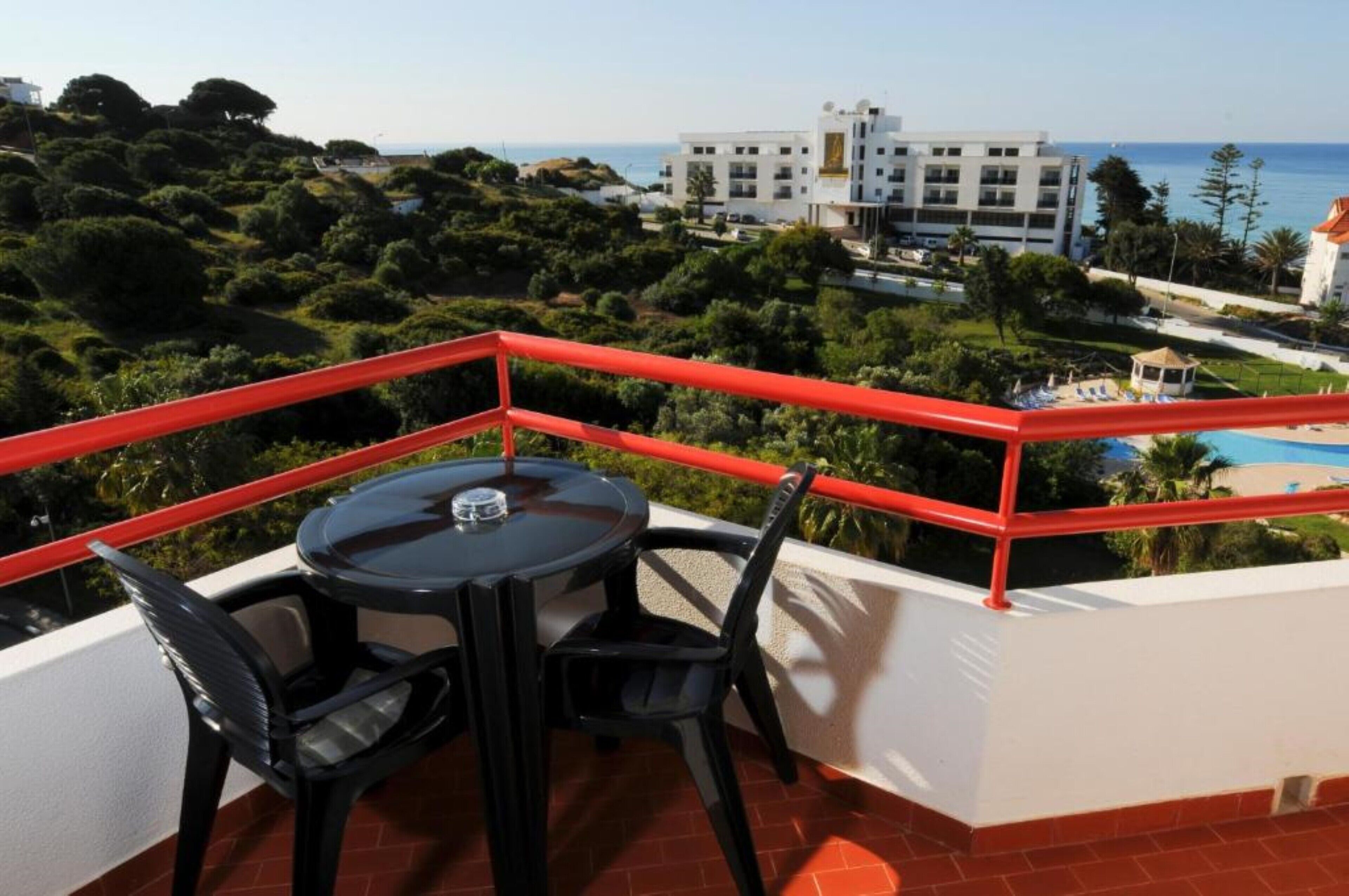 Ein Balkon mit Tisch und Stühlen, mit Blick auf einen Pool und ein Gebäude, das auf das Meer blickt.