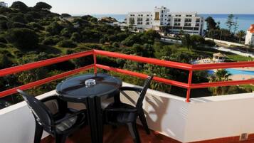 Un balcón con mesa y sillas, con vistas a una piscina y un edificio frente al mar.