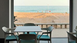 Habitación con vista a la playa a través de una ventana arqueada, que incluye una mesa y sillas.