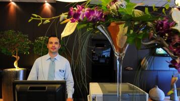 A reception desk with a computer, a large vase with flowers, and a potted plant.
