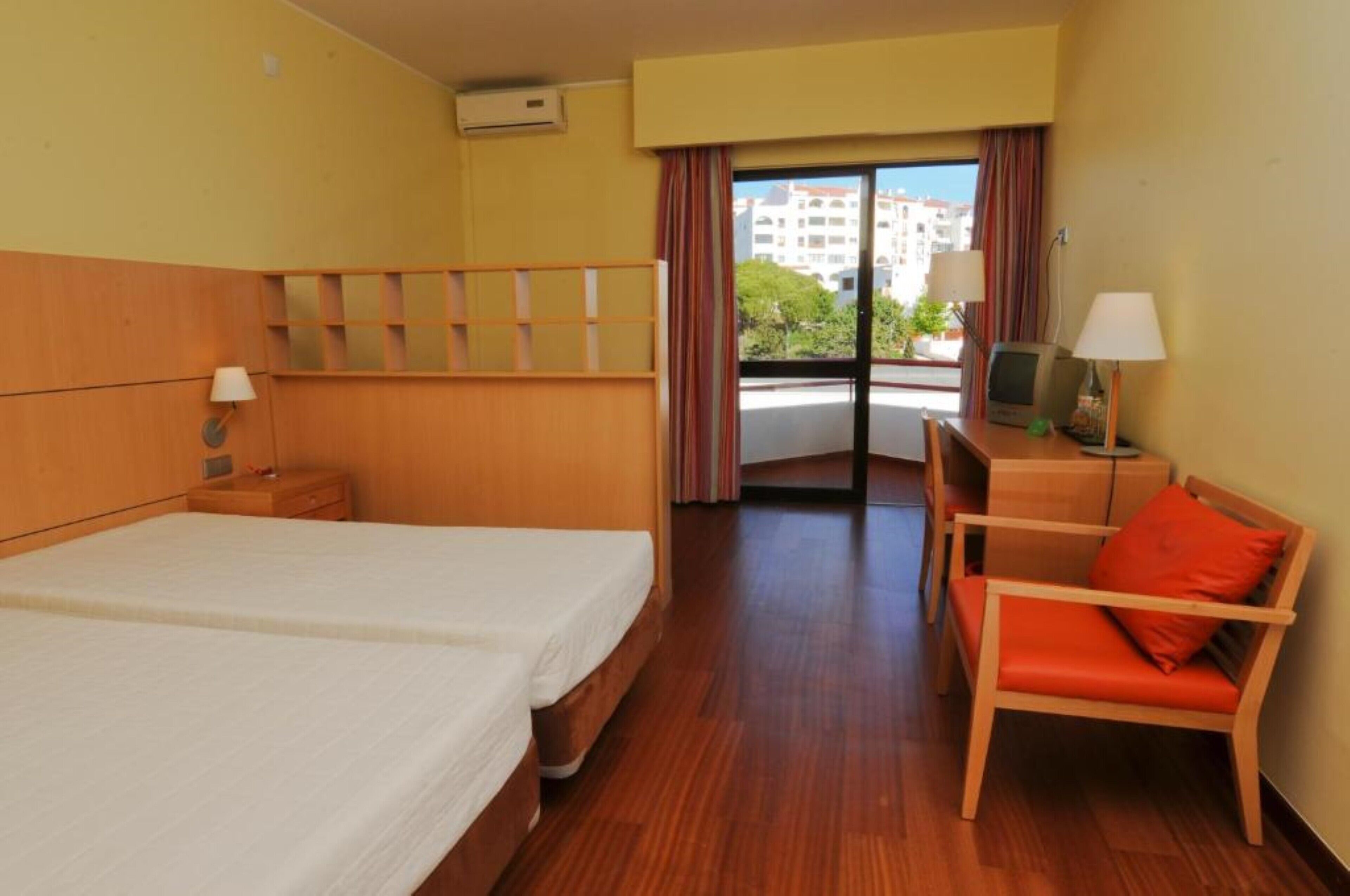 Habitación de hotel con dos camas, un escritorio con silla, televisor y ventana con cortinas.