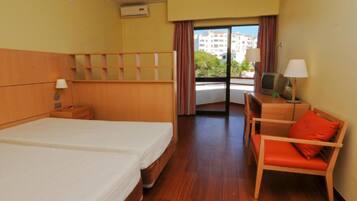 Habitación de hotel con dos camas, un escritorio con silla, televisor y ventana con cortinas.
