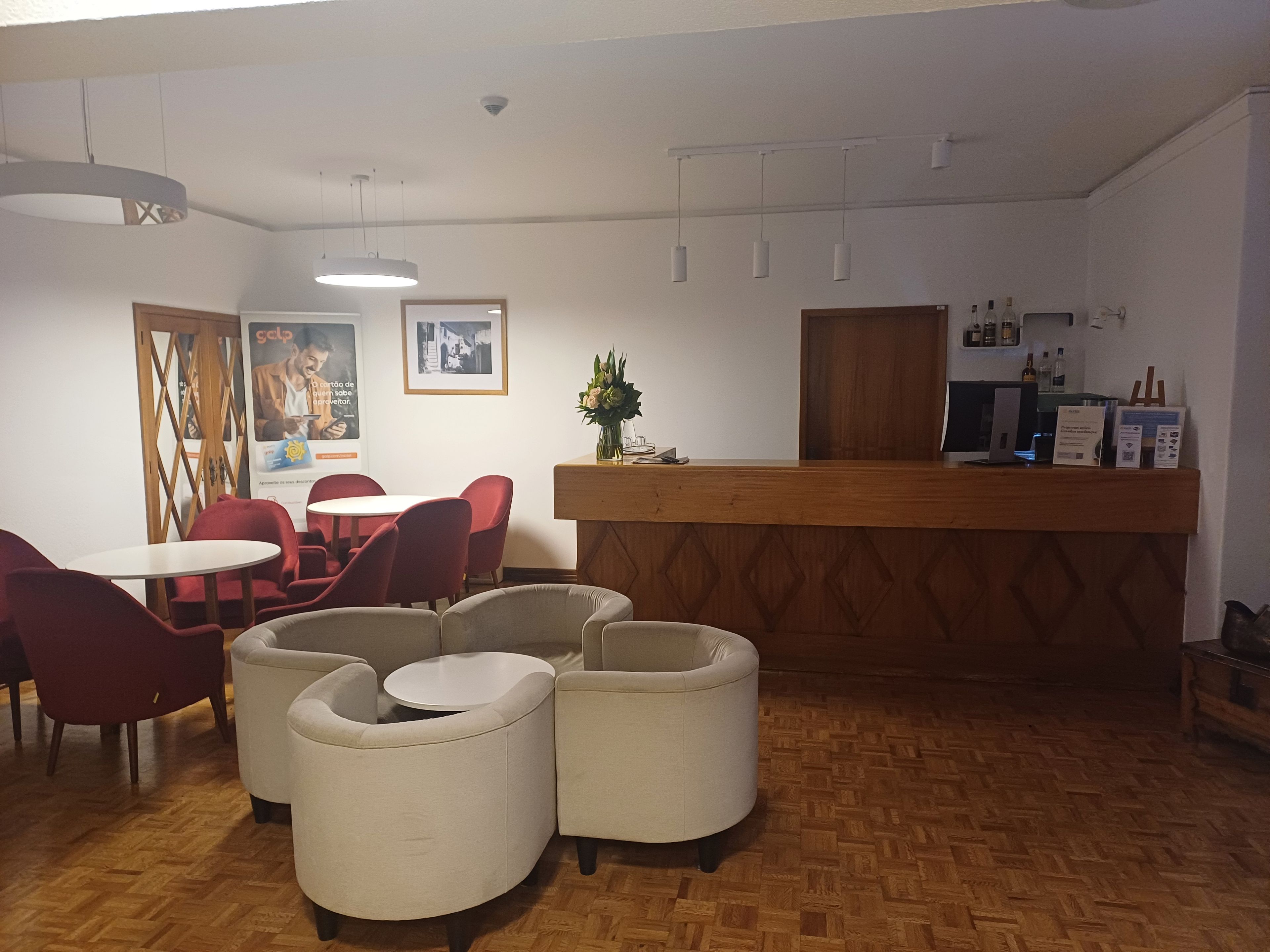 Zona de recepción con mostrador de madera, una computadora y una planta pequeña. Hay sillas rojas y una mesa blanca.