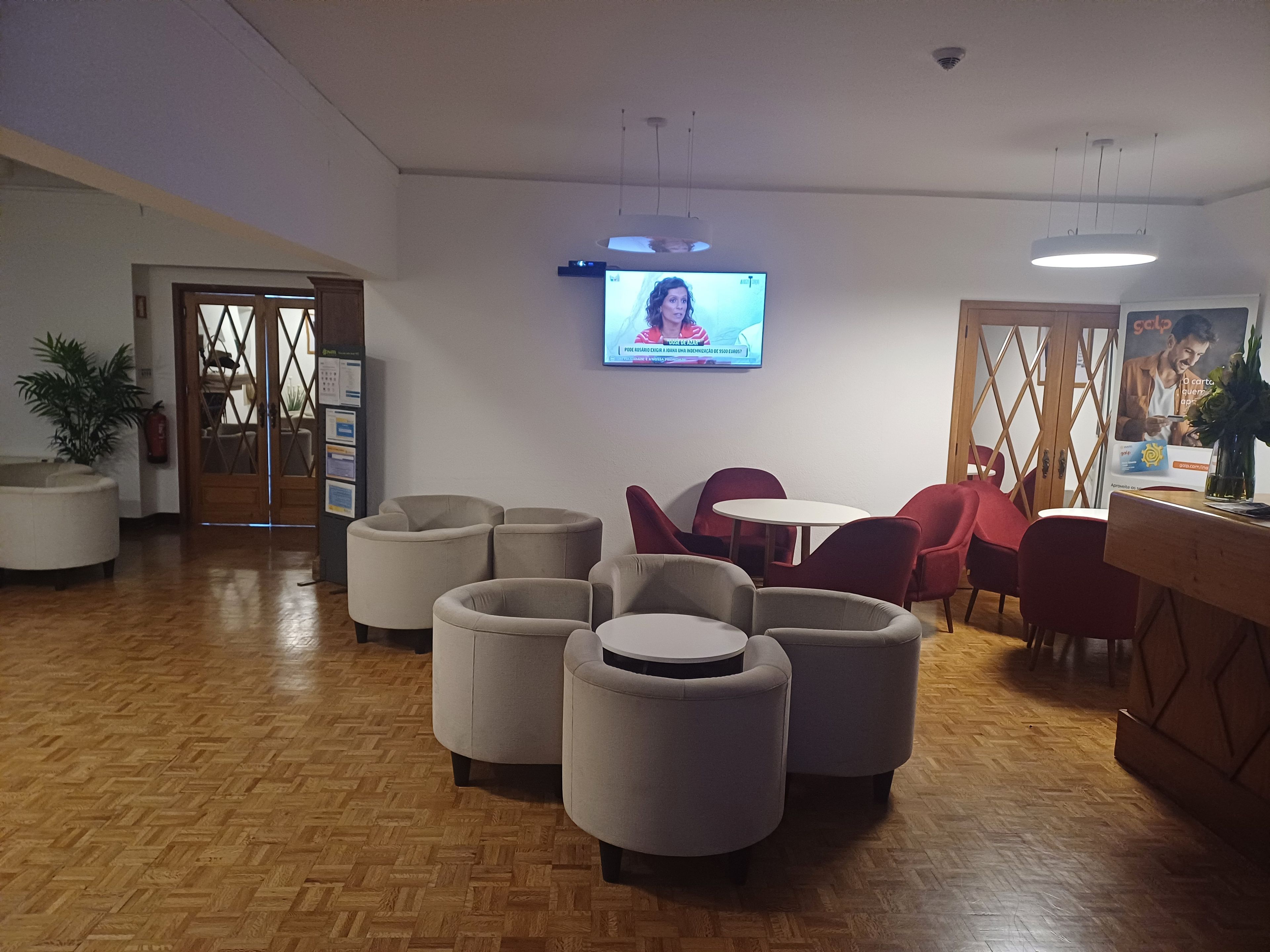 A lobby with a wooden herringbone floor, a television mounted on the wall, and a seating area with round tables and chairs.