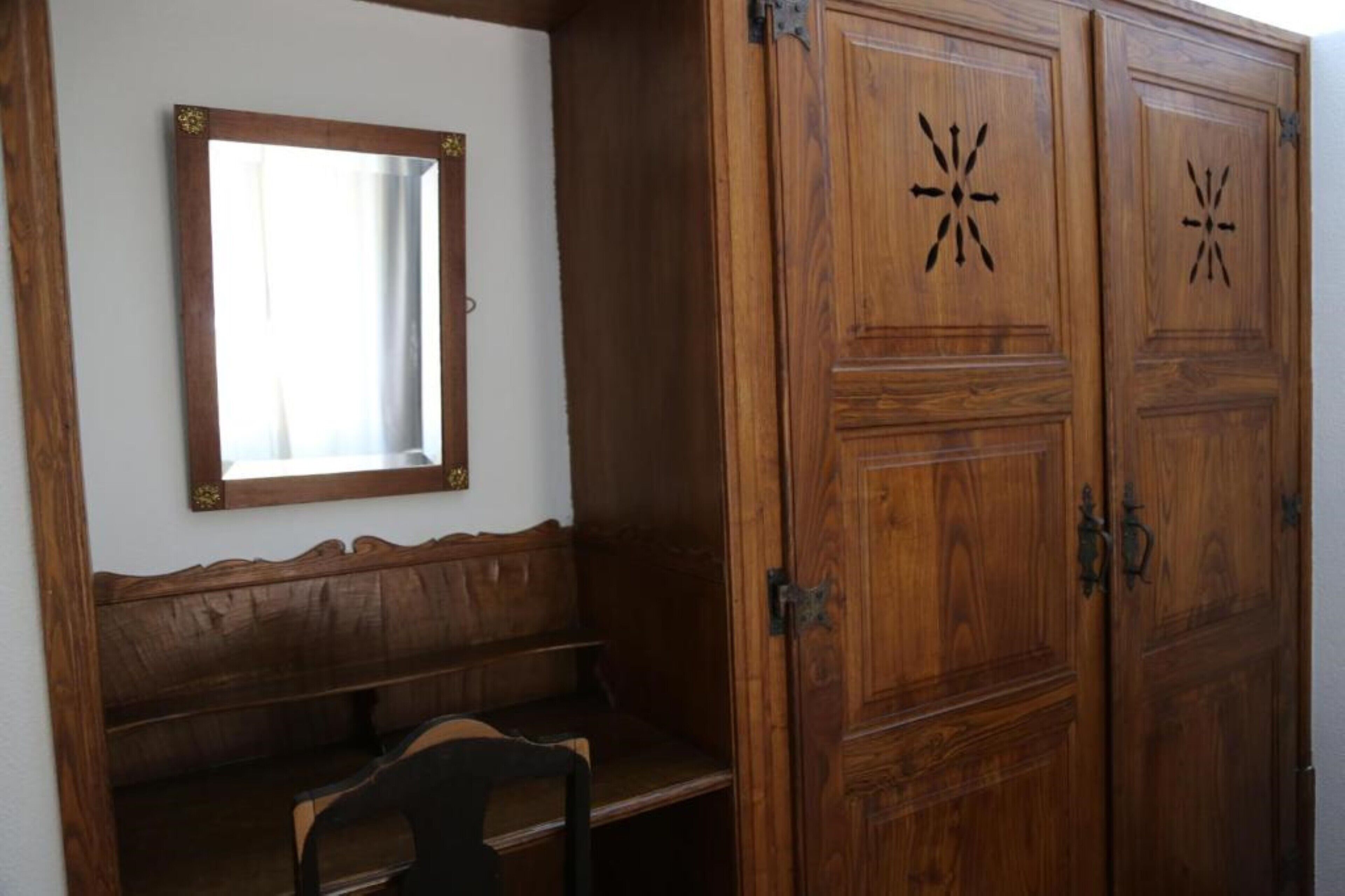 Une pièce comprenant un banc en bois, un miroir et deux portes en bois ornées de motifs en forme d’étoile.