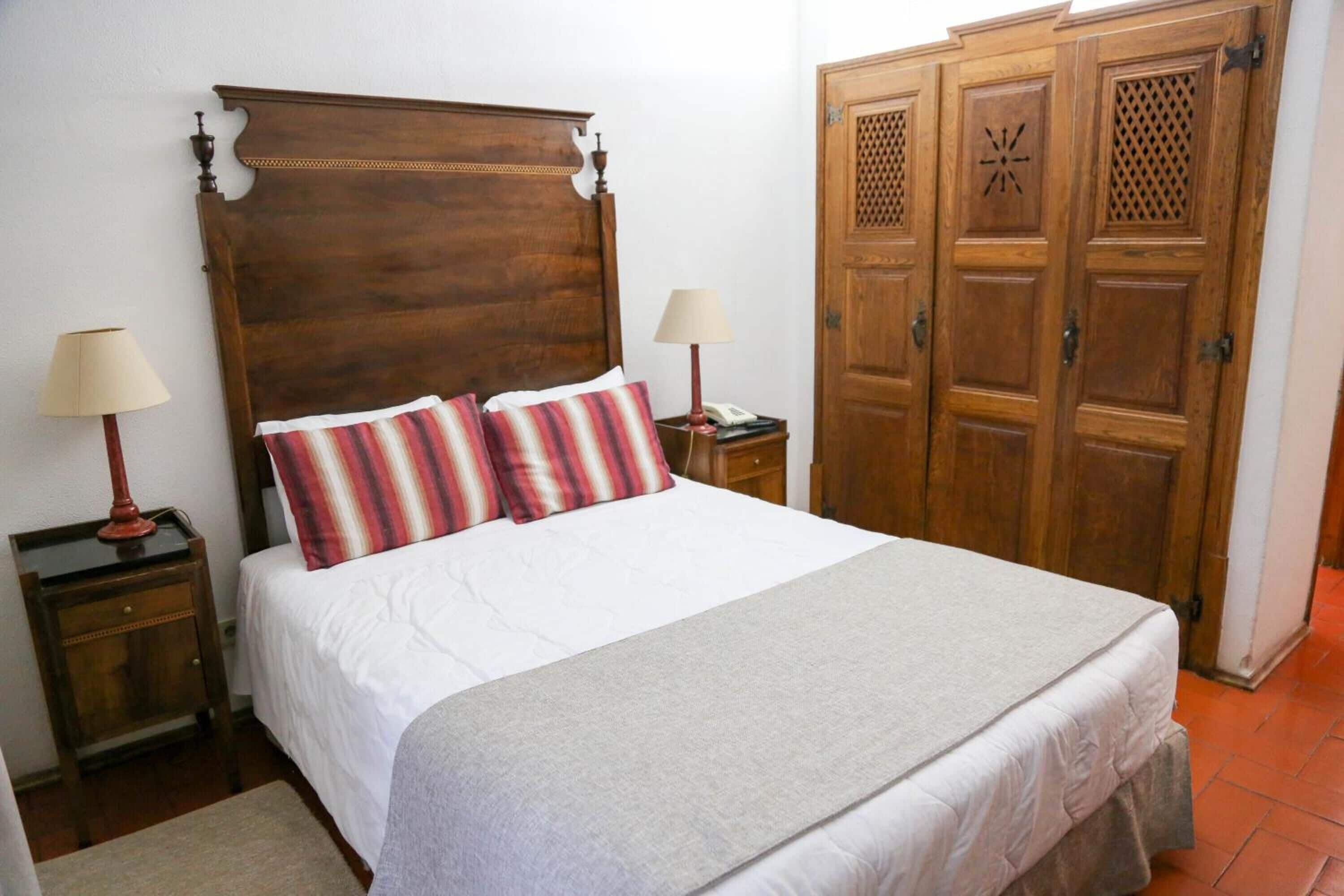 Un dormitorio con cama de madera, dos mesitas de noche con lámparas, un armario y una alfombra.