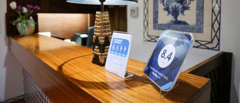 A reception desk with a lamp, a framed artwork, and a digital sign displaying a rating.