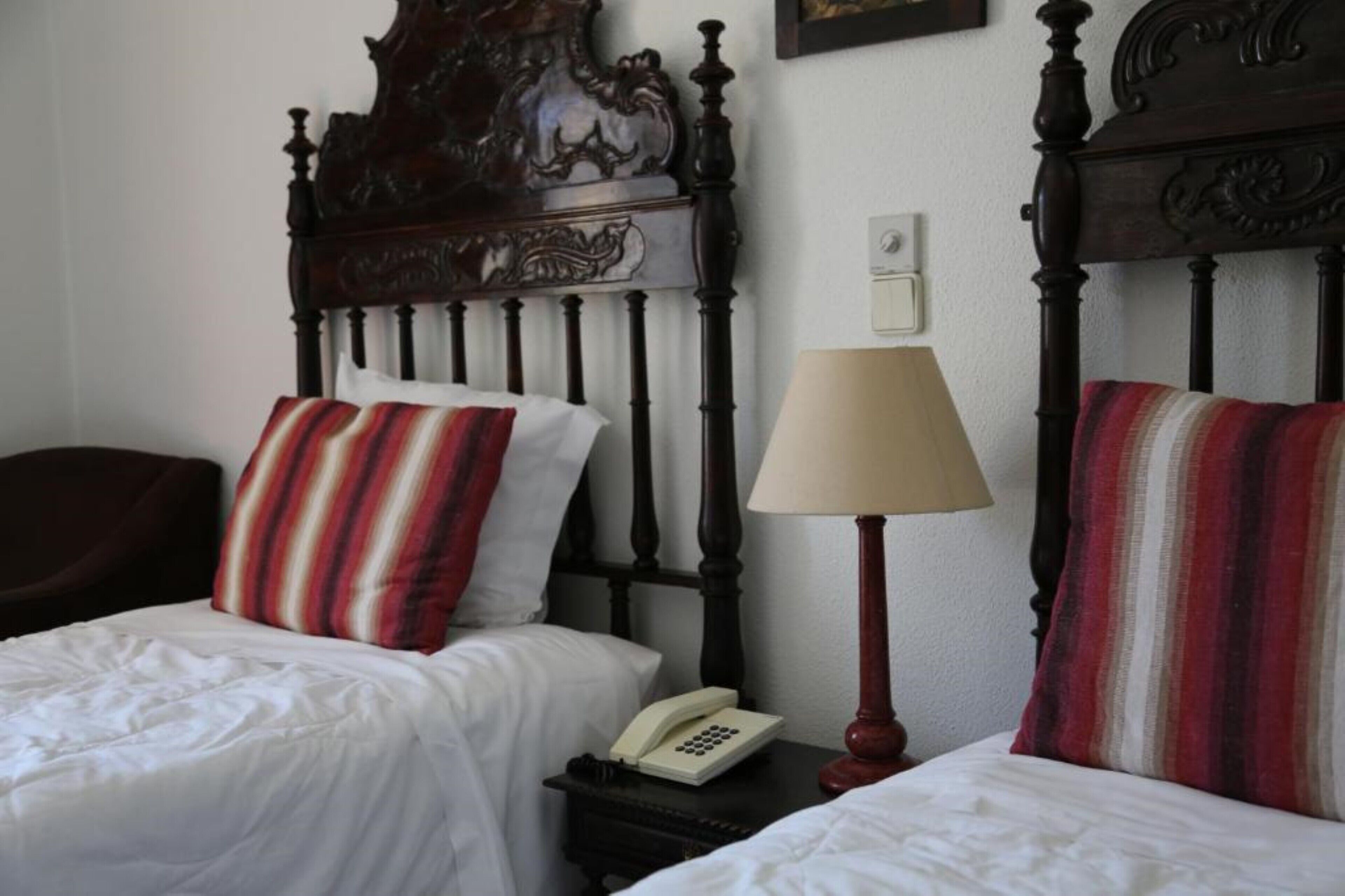 A double bed with a wooden headboard, two pillows, a bedside lamp, and a telephone on a nightstand.