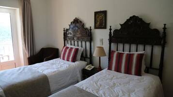 Una habitación de hotel con dos camas individuales, cabecero de madera, mesita de noche con lámpara, teléfono y ventana con cortinas.
