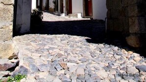 A stone archway leading to a white building with a red door, a cobblestone street, and a clear blue sky. - INATEL Castelo de Vide (Castelo de Vide)