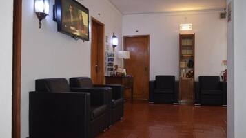 A lobby with a reception desk, two black sofas, a wooden door, and a wall-mounted TV.