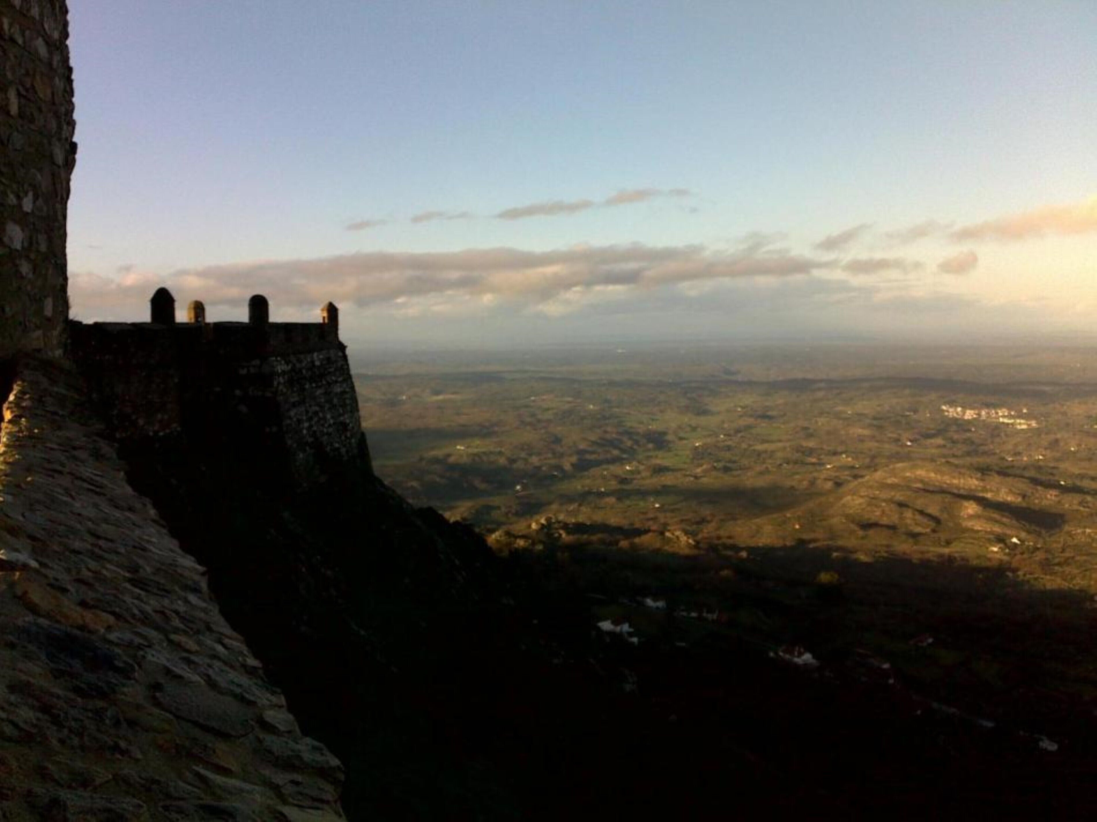 Un muro de piedra con vista a un valle y edificios lejanos.