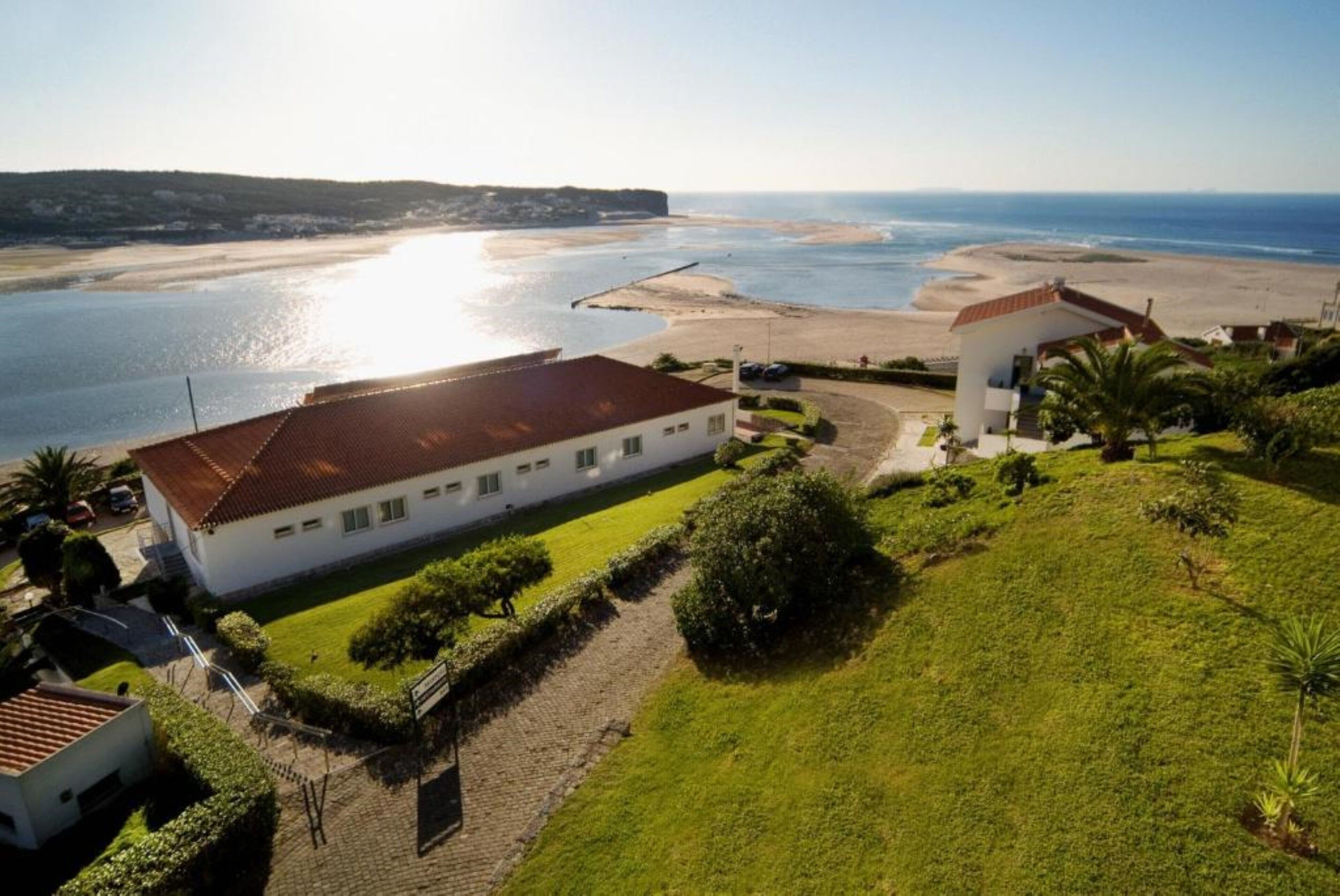A coastal building with a red roof, surrounded by a well-maintained lawn and a paved driveway.