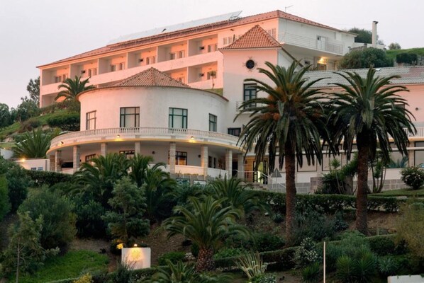A multi-story hotel with a curved balcony, palm trees, and a well-maintained garden. - INATEL Foz do Arelho (Caldas da Rainha)