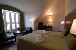 A hotel room with two beds, a desk, a chair, and a window with curtains. - INATEL Foz do Arelho (Caldas da Rainha)