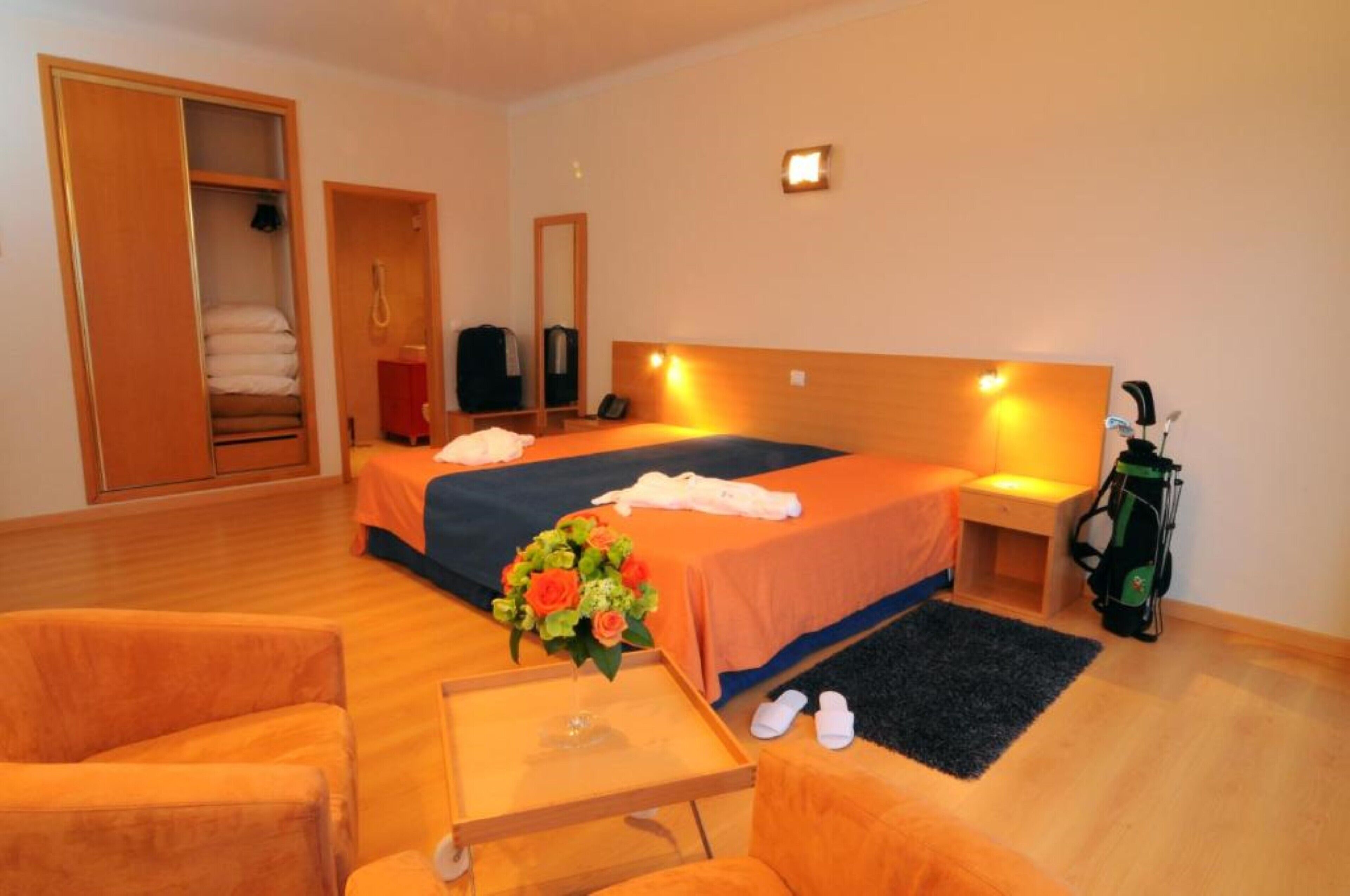 Ein Hotelzimmer mit Bett, Schreibtisch, Stuhl, Kleiderschrank und einer Golftasche.