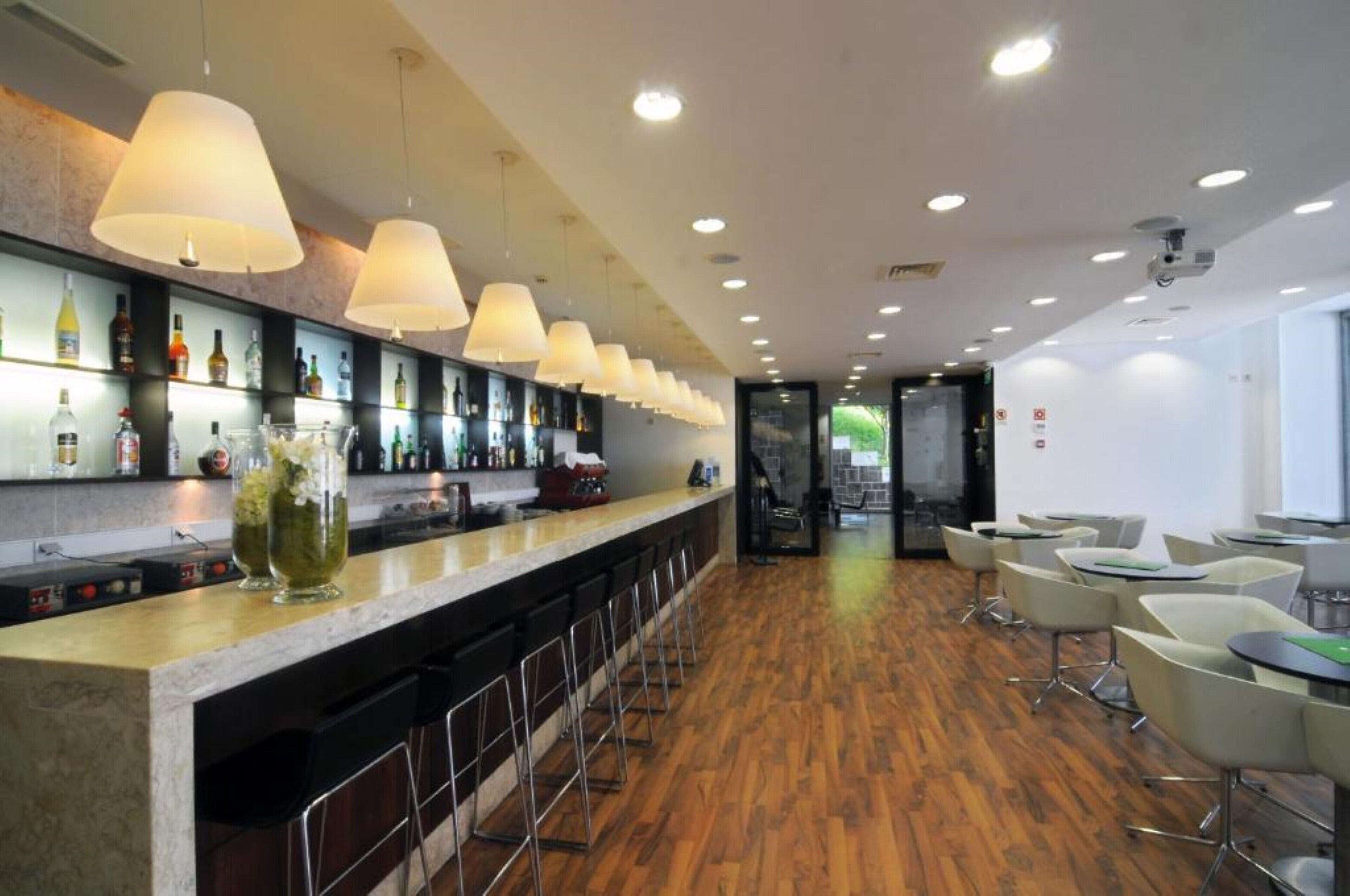 Uma área de bar moderna com um balcão comprido, várias luminárias pendentes e uma variedade de garrafas em prateleiras.