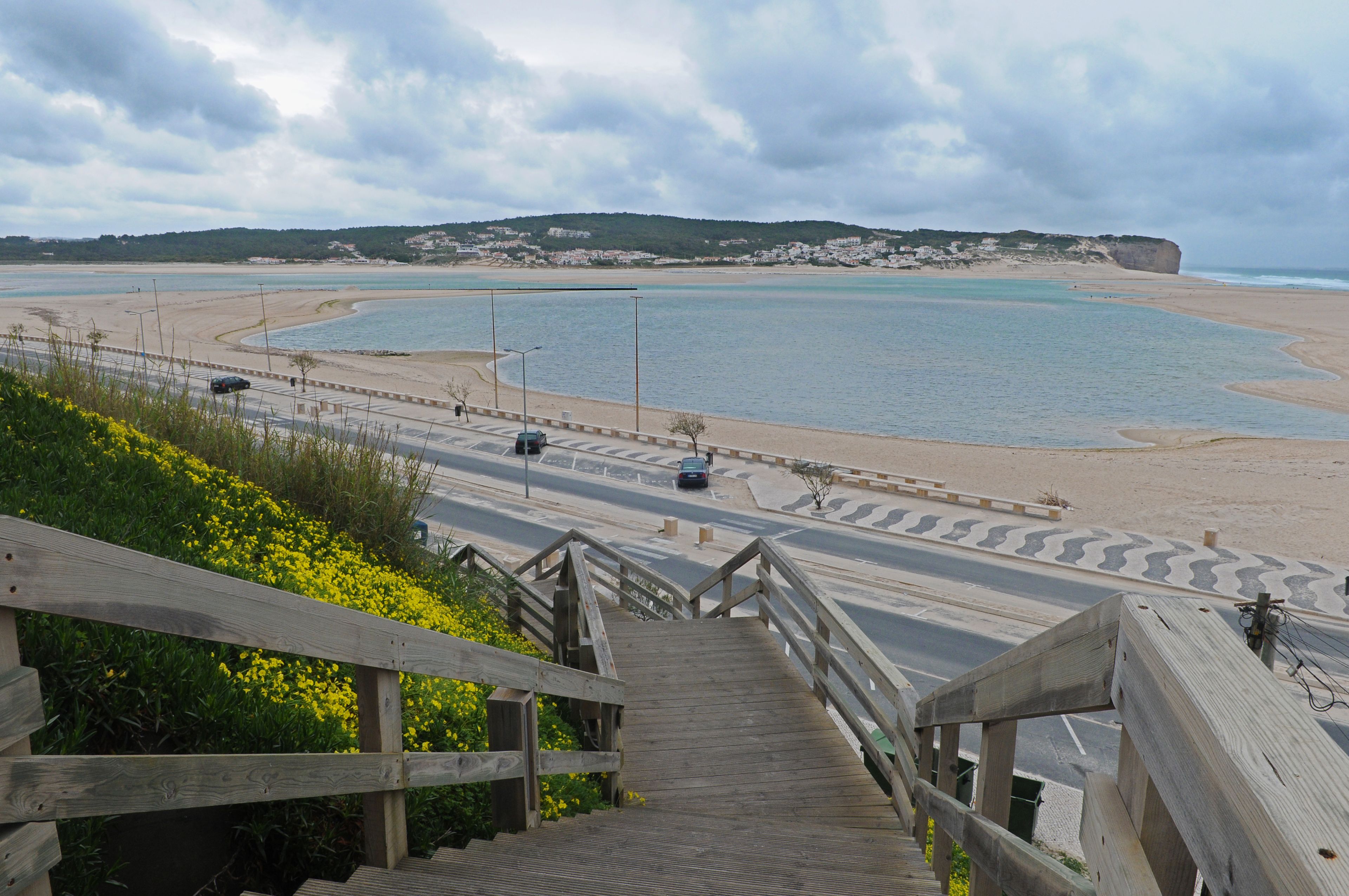 Eine Küstenstraße führt zu einem Strand mit einer Holztreppe und freiem Blick auf das Meer.