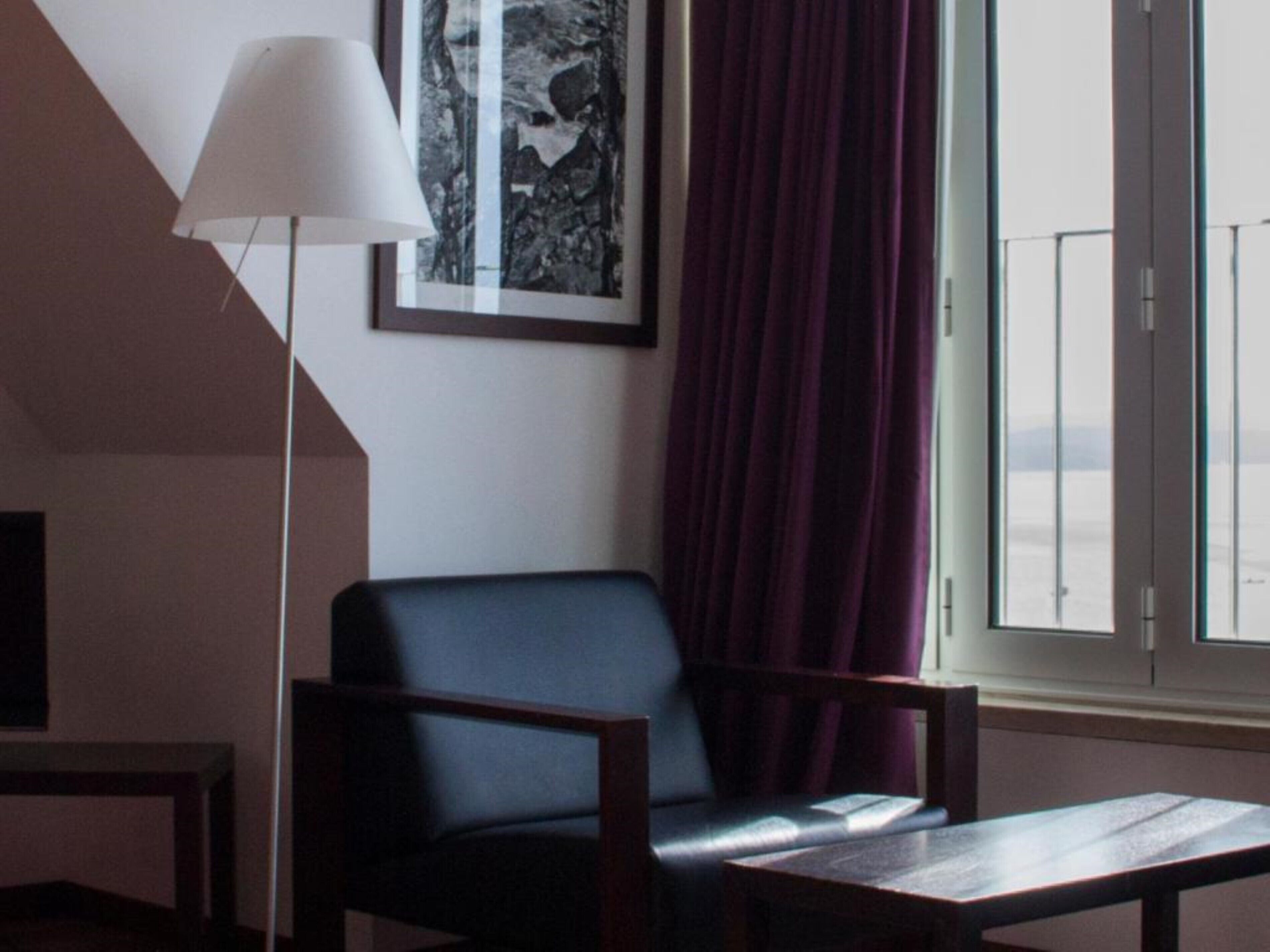 A modern room with a dark leather chair, a small table, a floor lamp, and a large window with curtains.