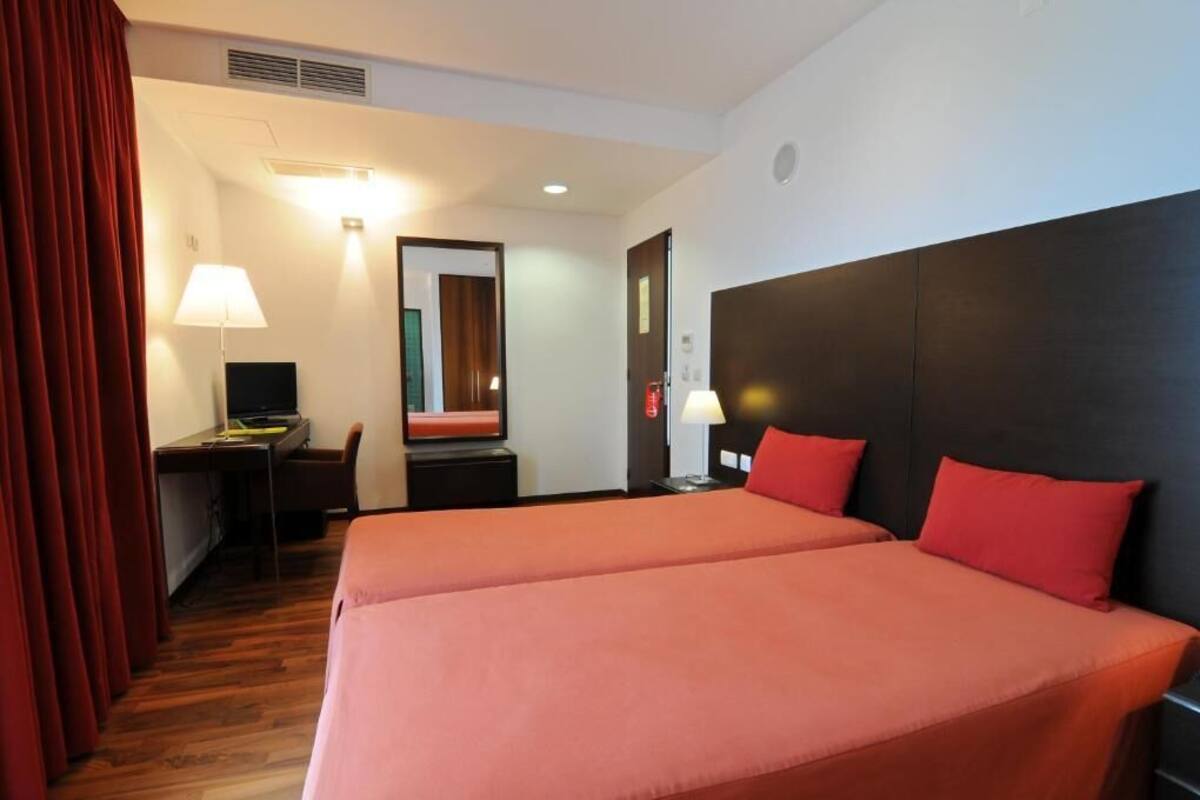 Ein Hotelzimmer mit zwei Betten, einem Schreibtisch mit Stuhl, einem Computer und einer Lampe.