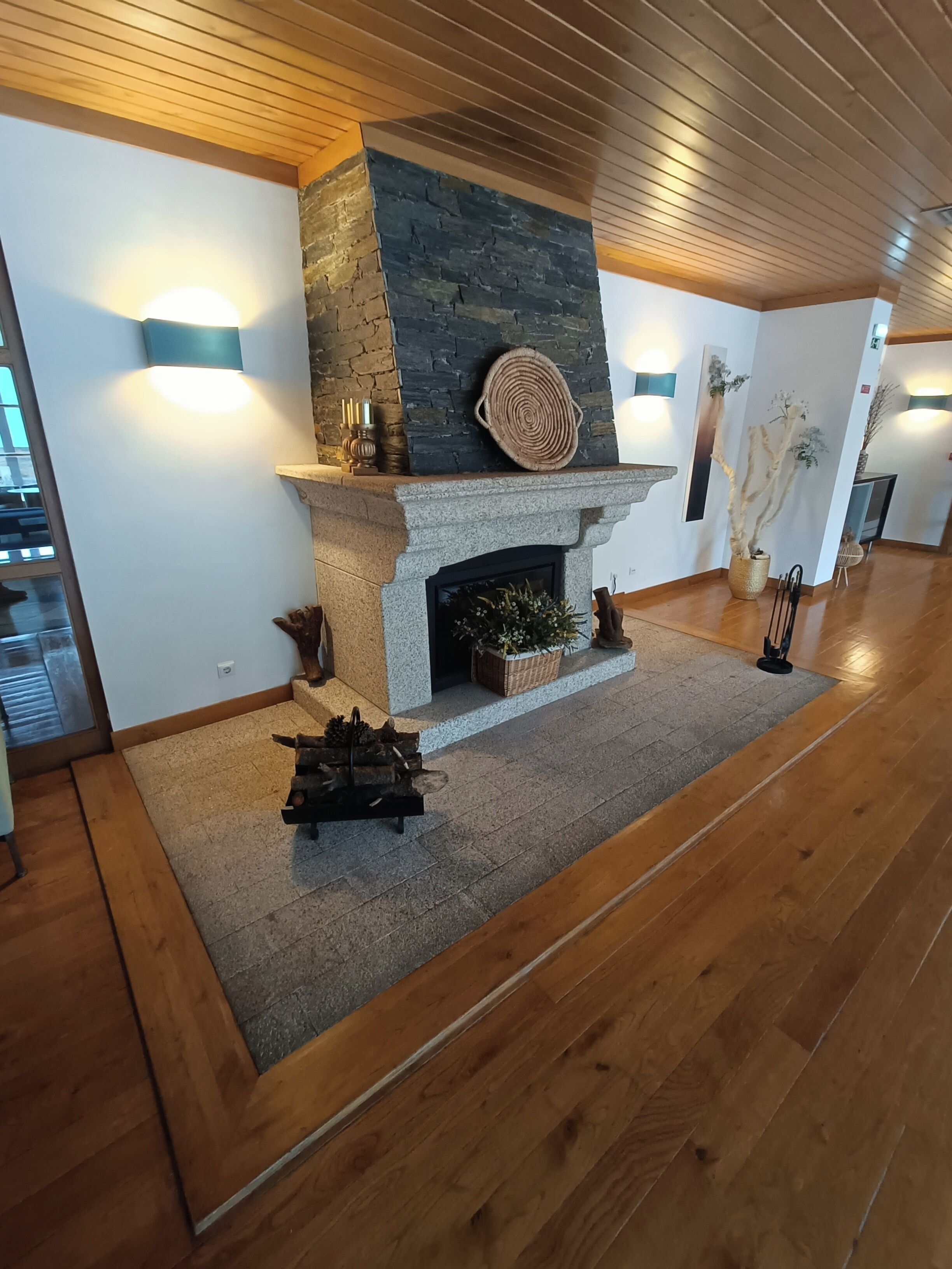 A modern interior with a stone fireplace, wooden flooring, and decorative wall sconces.