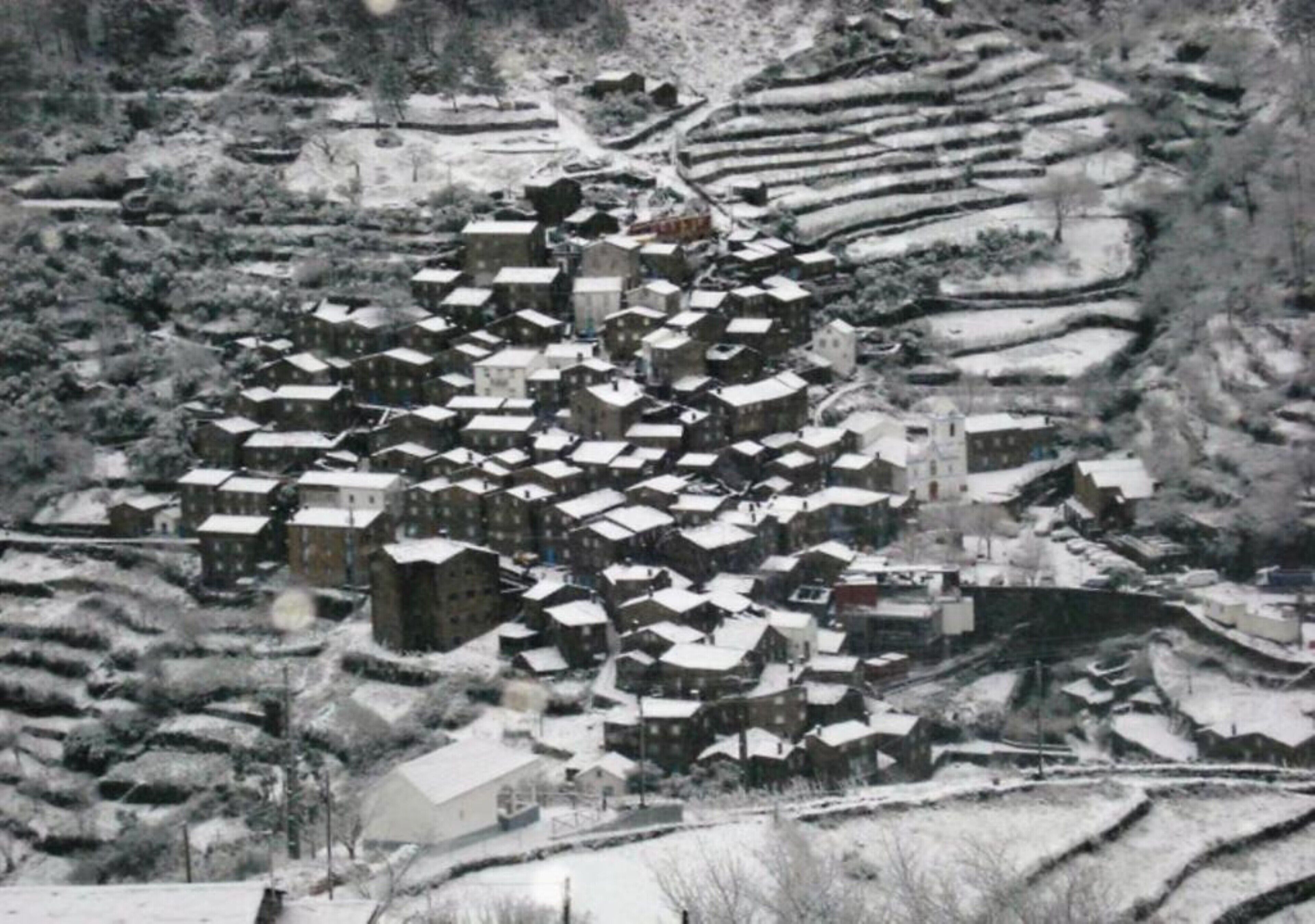 Un pueblo cubierto de nieve con casas escalonadas y una iglesia destacada.
