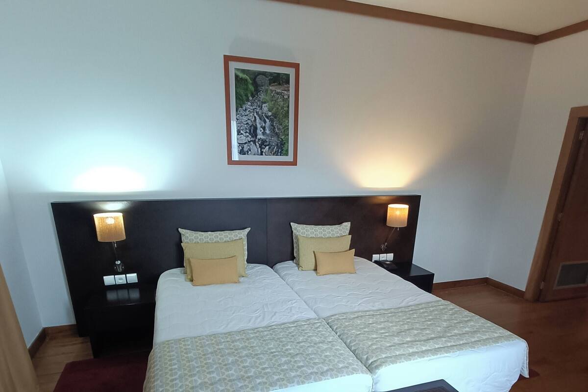 A bedroom with a large bed, two bedside tables with lamps, a wooden floor, and a framed picture on the wall.