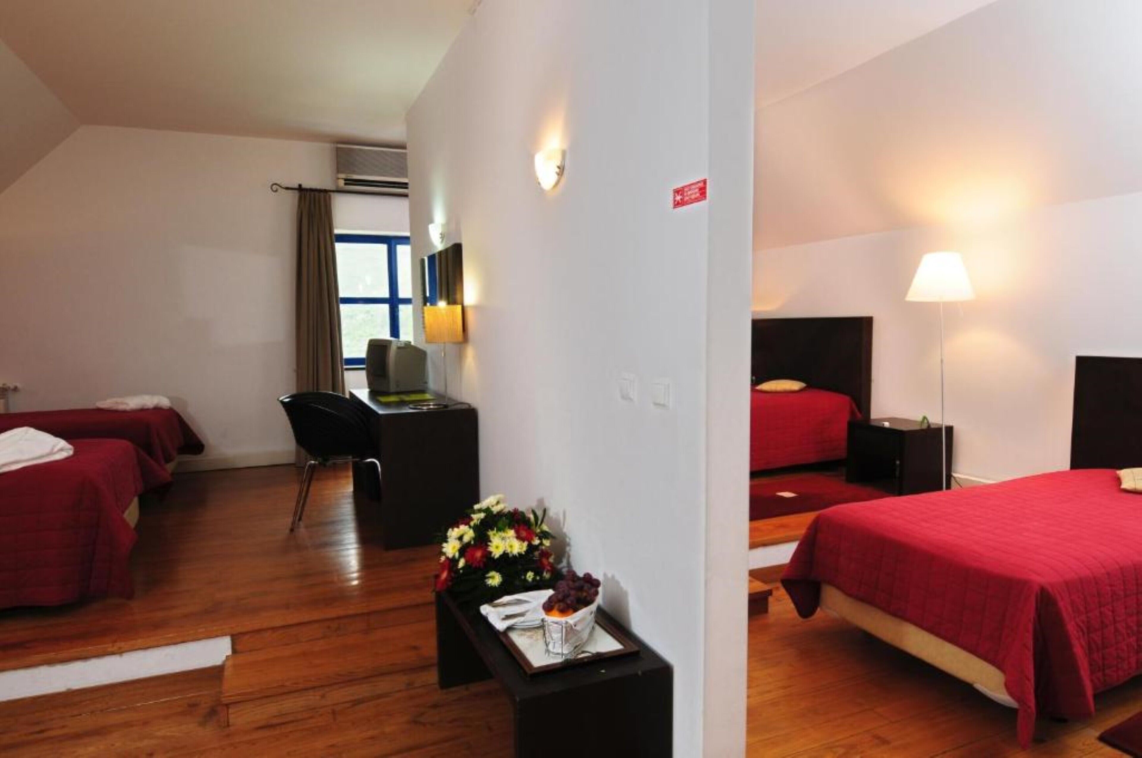 Une chambre d’hôtel avec deux lits, un bureau, une chaise et une petite table agrémentée de fleurs.
