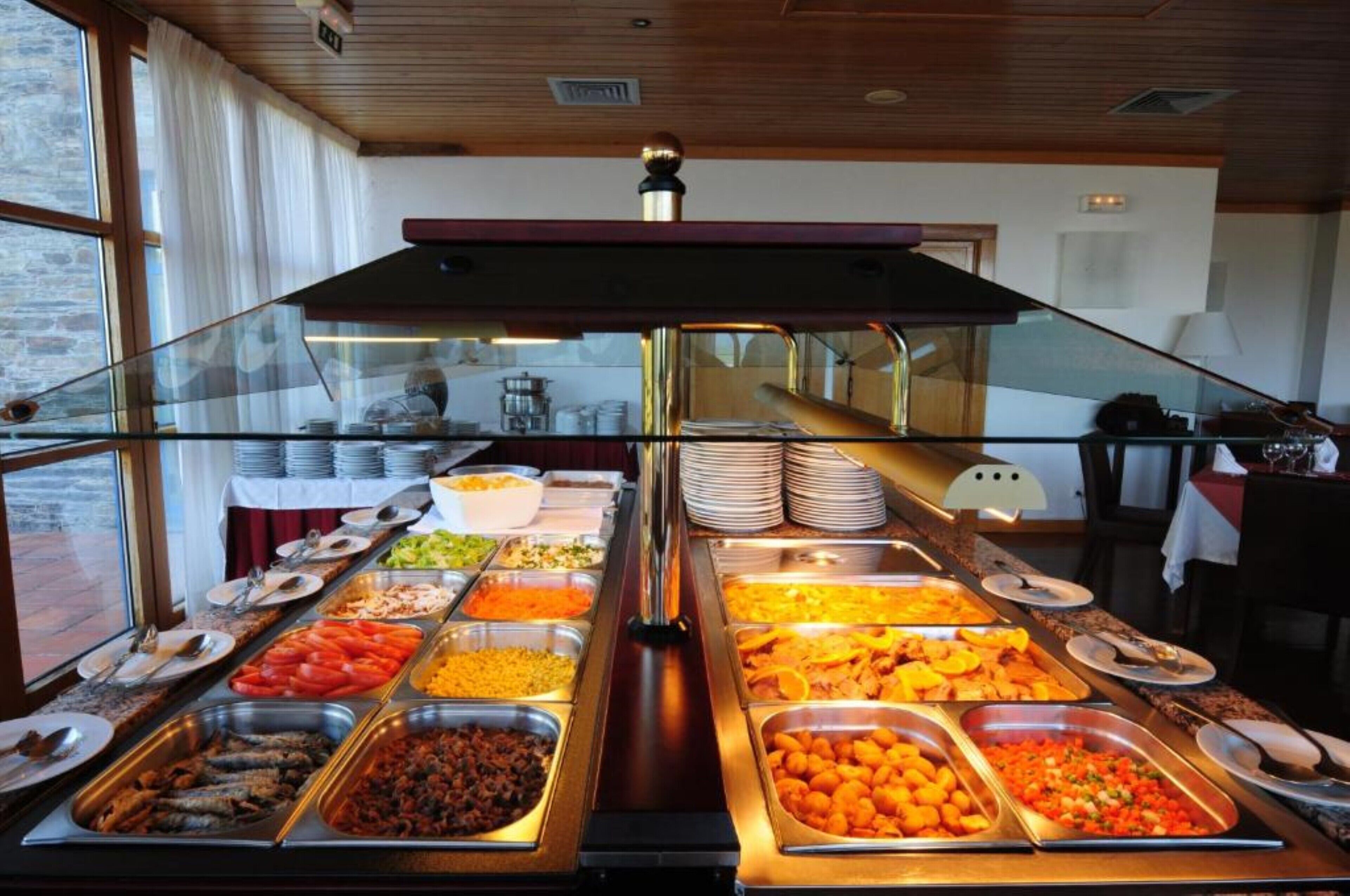 A buffet with various food options, a glass partition, and a view of the room with a fireplace and a table with a lamp.