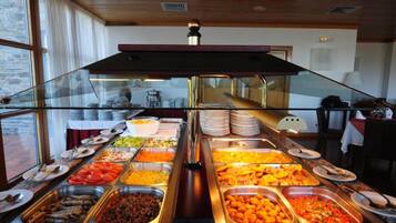 A buffet with various food options, a glass partition, and a view of the room with a fireplace and a table with a lamp.