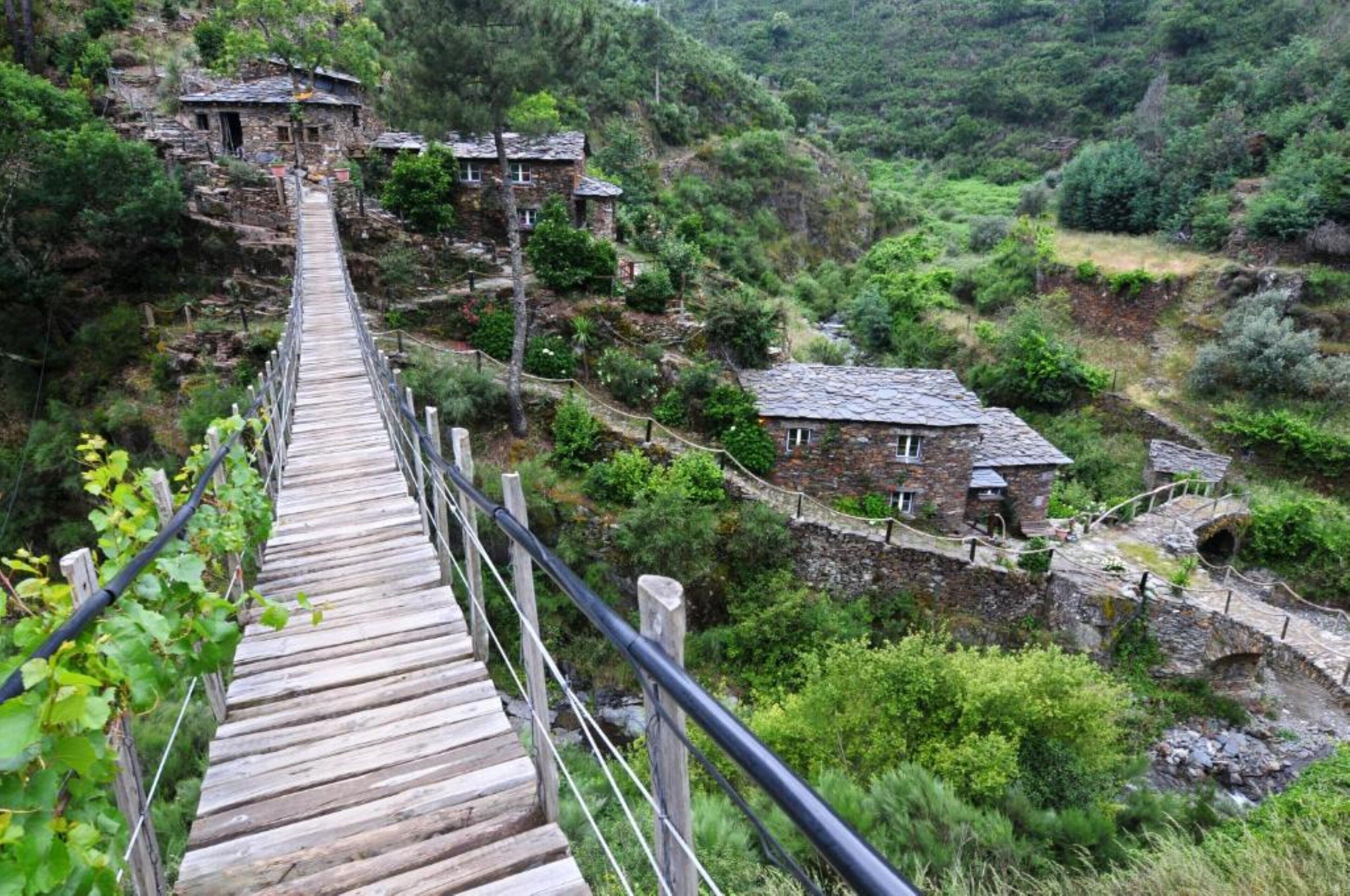 A wooden bridge leading to a stone village with traditional houses.
