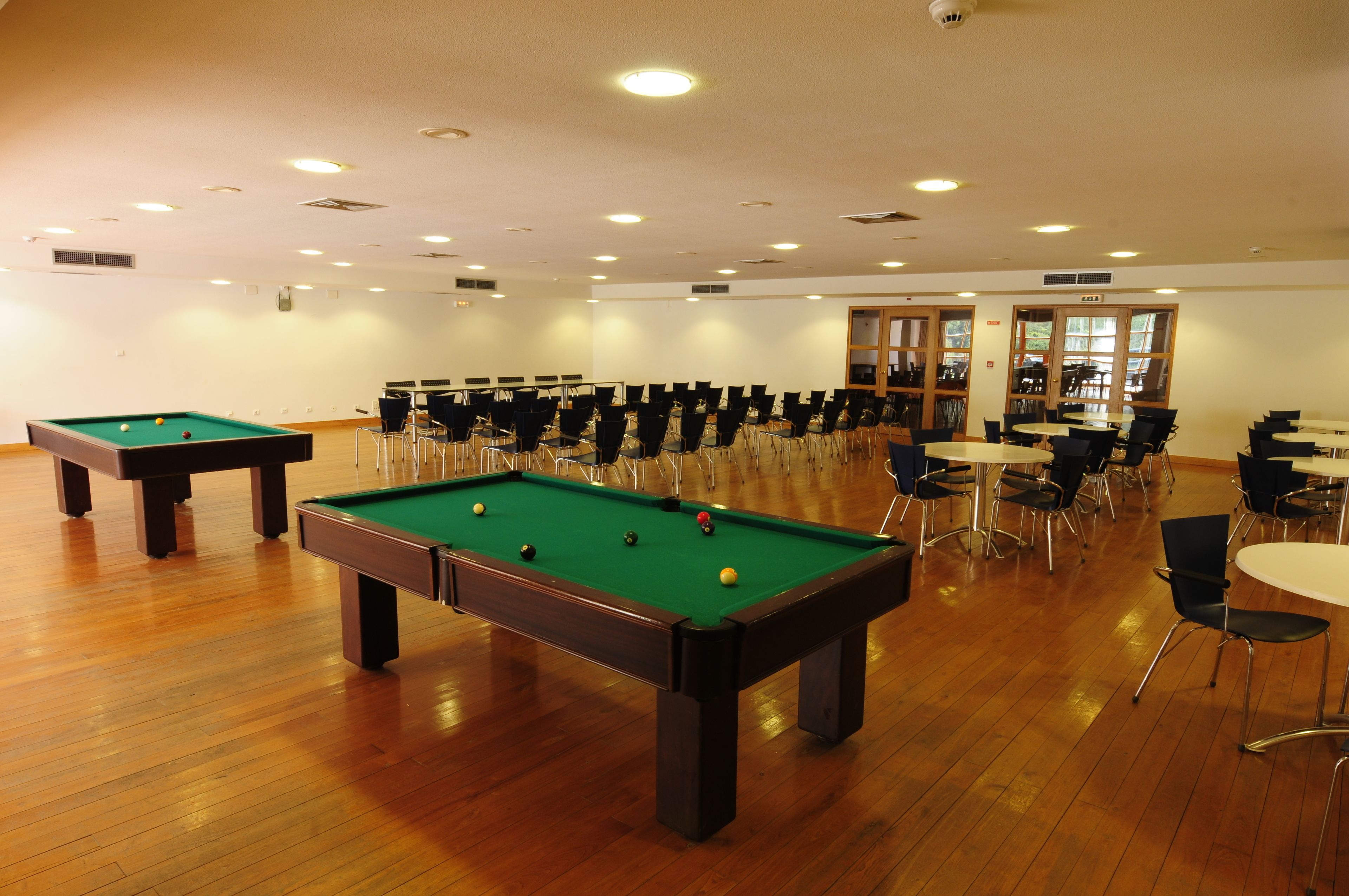 Une salle de billard équipée de deux tables de billard, de chaises et de tables disposées de manière à favoriser la convivialité.