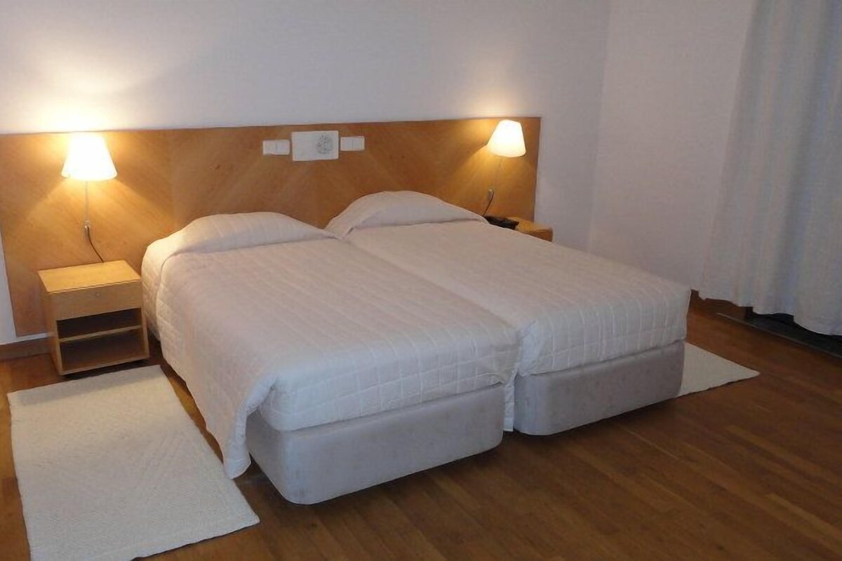 Una cama doble con dos almohadas, una mesita de noche y otra mesilla auxiliar.